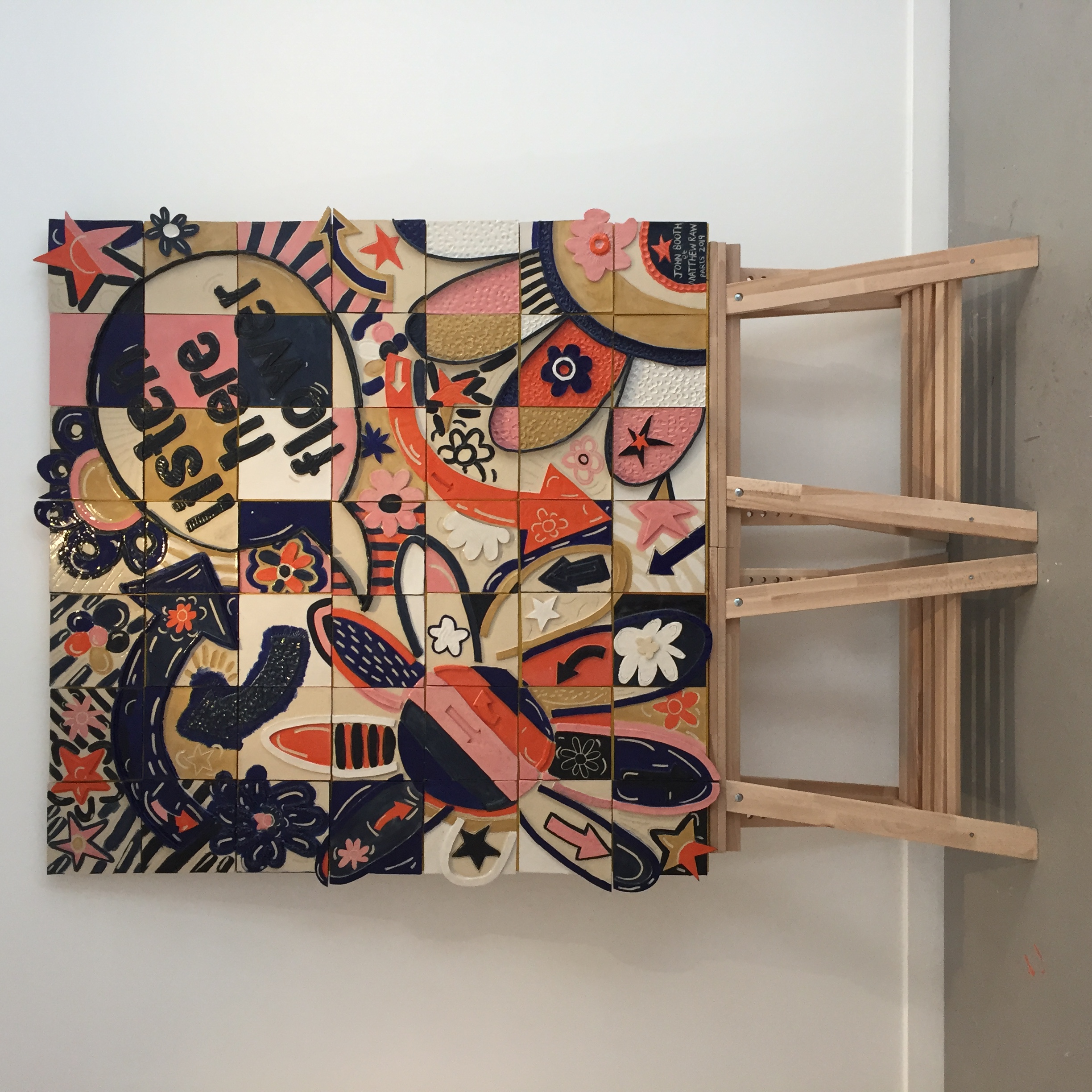 A colourful tiled mural with the words ‘listen here flower’ stands on two trestles