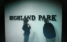Two people stand in front of the words ‘HIGHLAND PARK’ on a wall