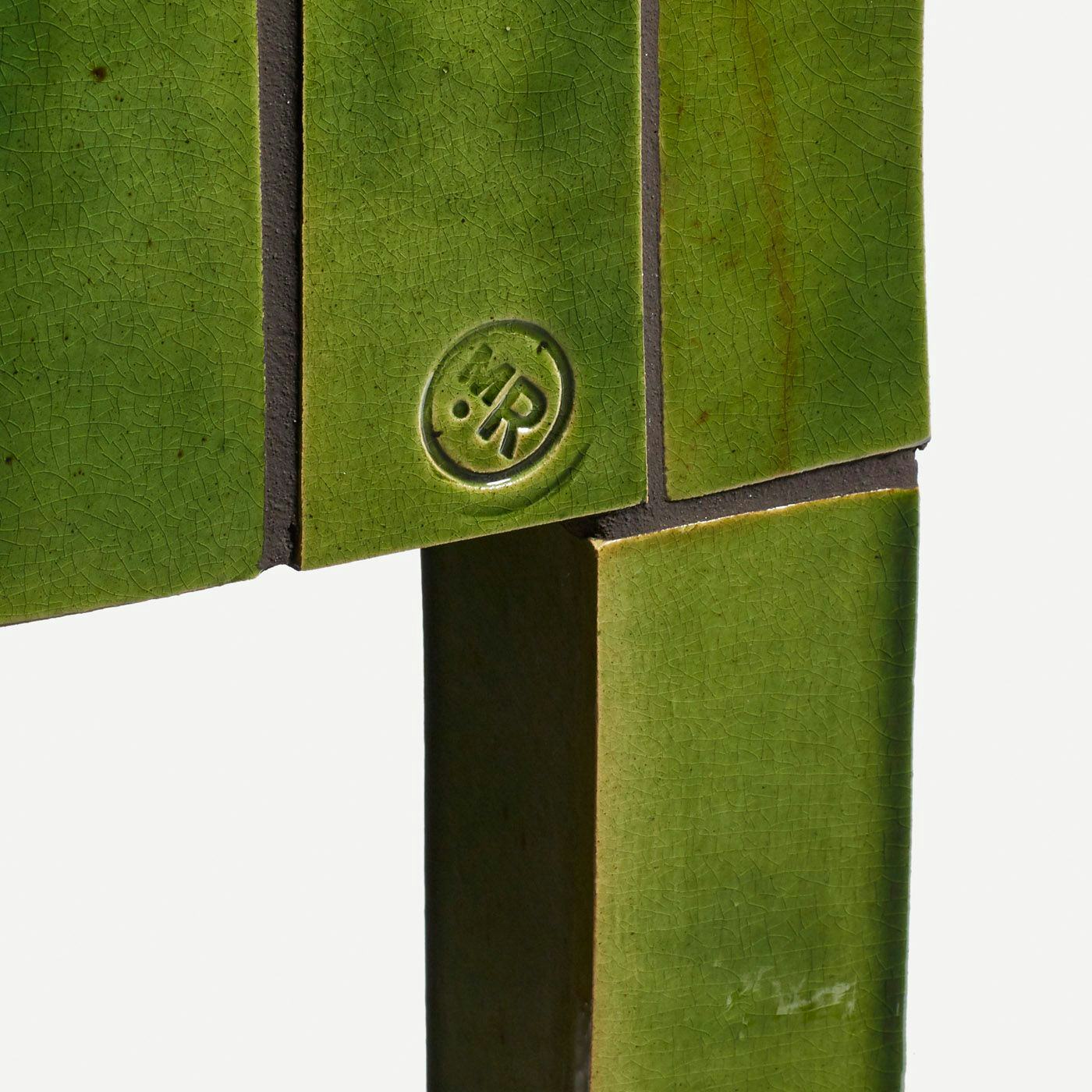 A detail of a green tiled cupboard showing the makers mark: a circle with the initials M R