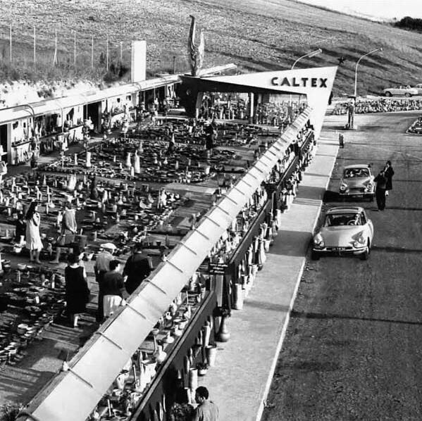 A black and white photograph showing old two cars outside a venue with a sign saying ‘CALTEX’