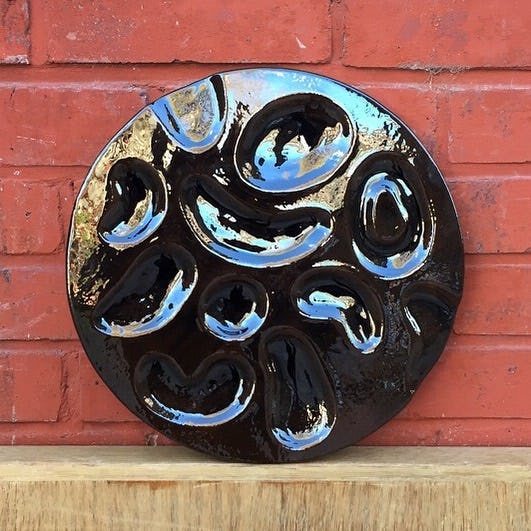 A circular ceramic artwork sits on a wooden plinth in front of a red brick wall