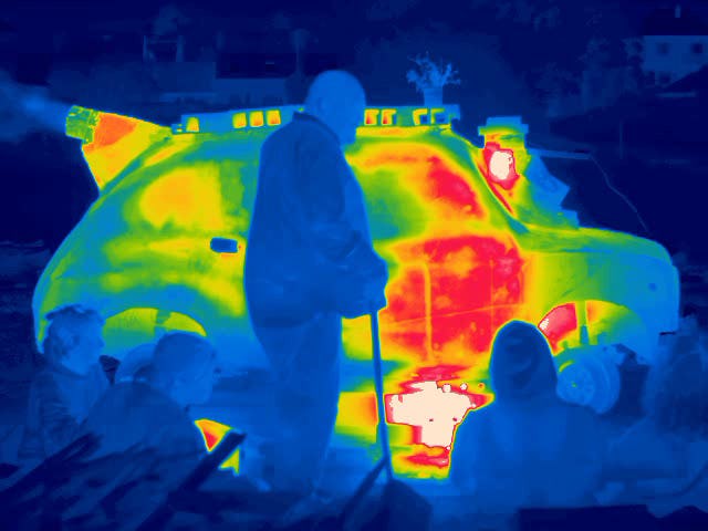 A still from a thermal imaging camera showing a group of people in front of a very hot car