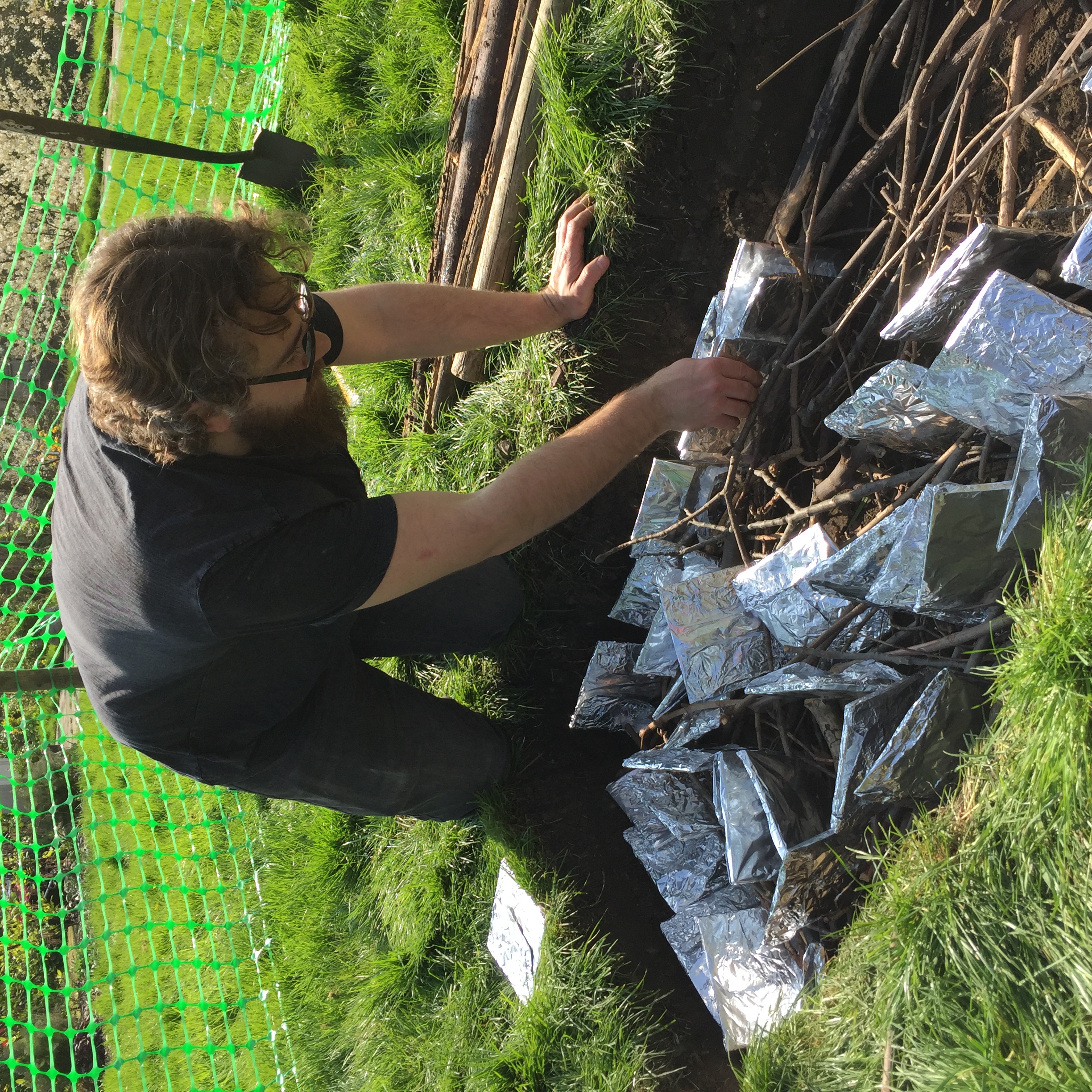 A man places clay tiles into a pit full of branches in preparation for firing them