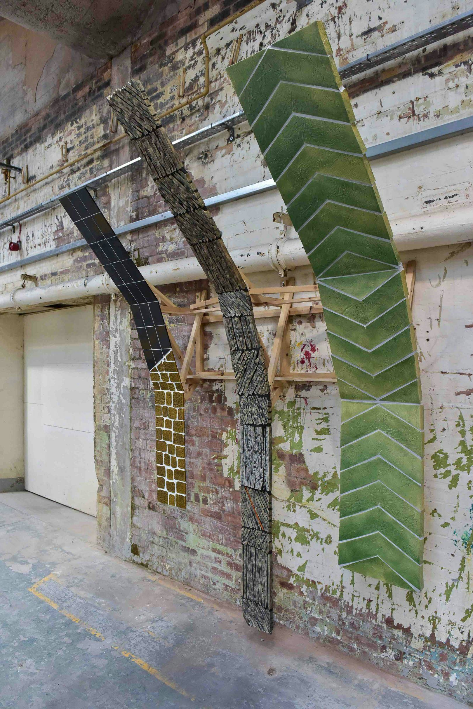 Three large, tiled artworks hang in an old building and curve up and over away from the wall
