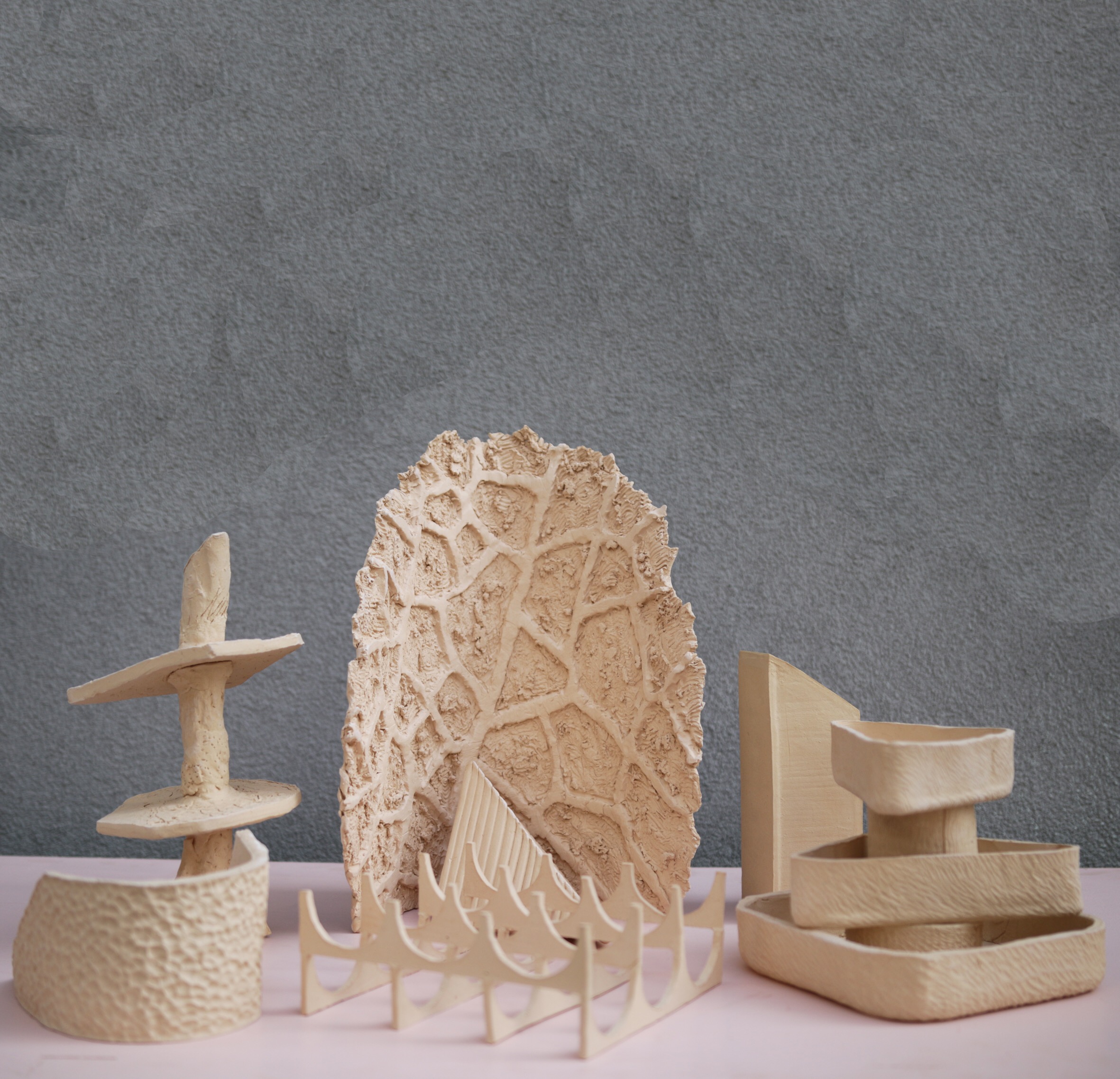 A variety of different ceramics on a pink table in front of a grey wall