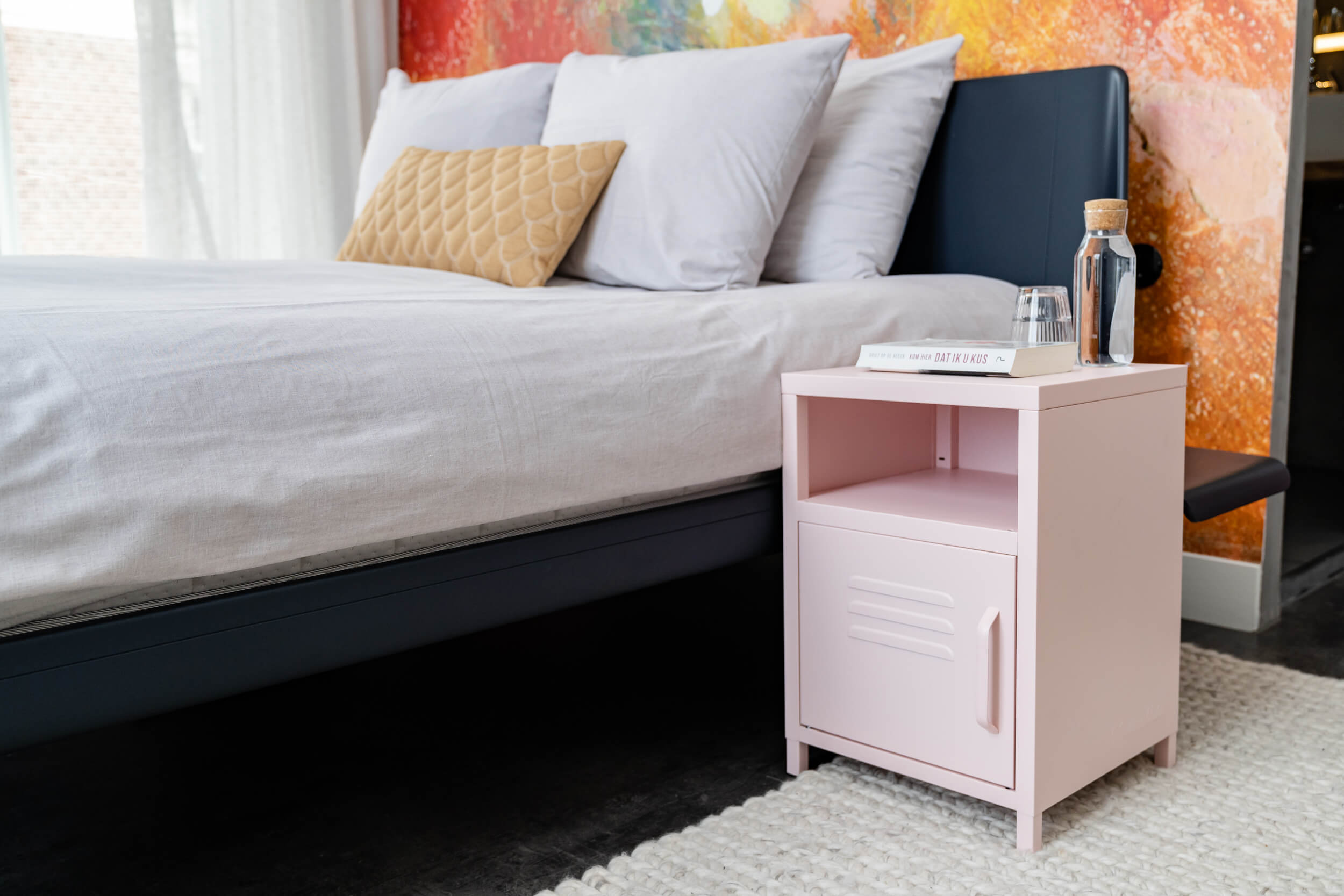 Poederroze nachtkastje op een hotelkamer naast het bed