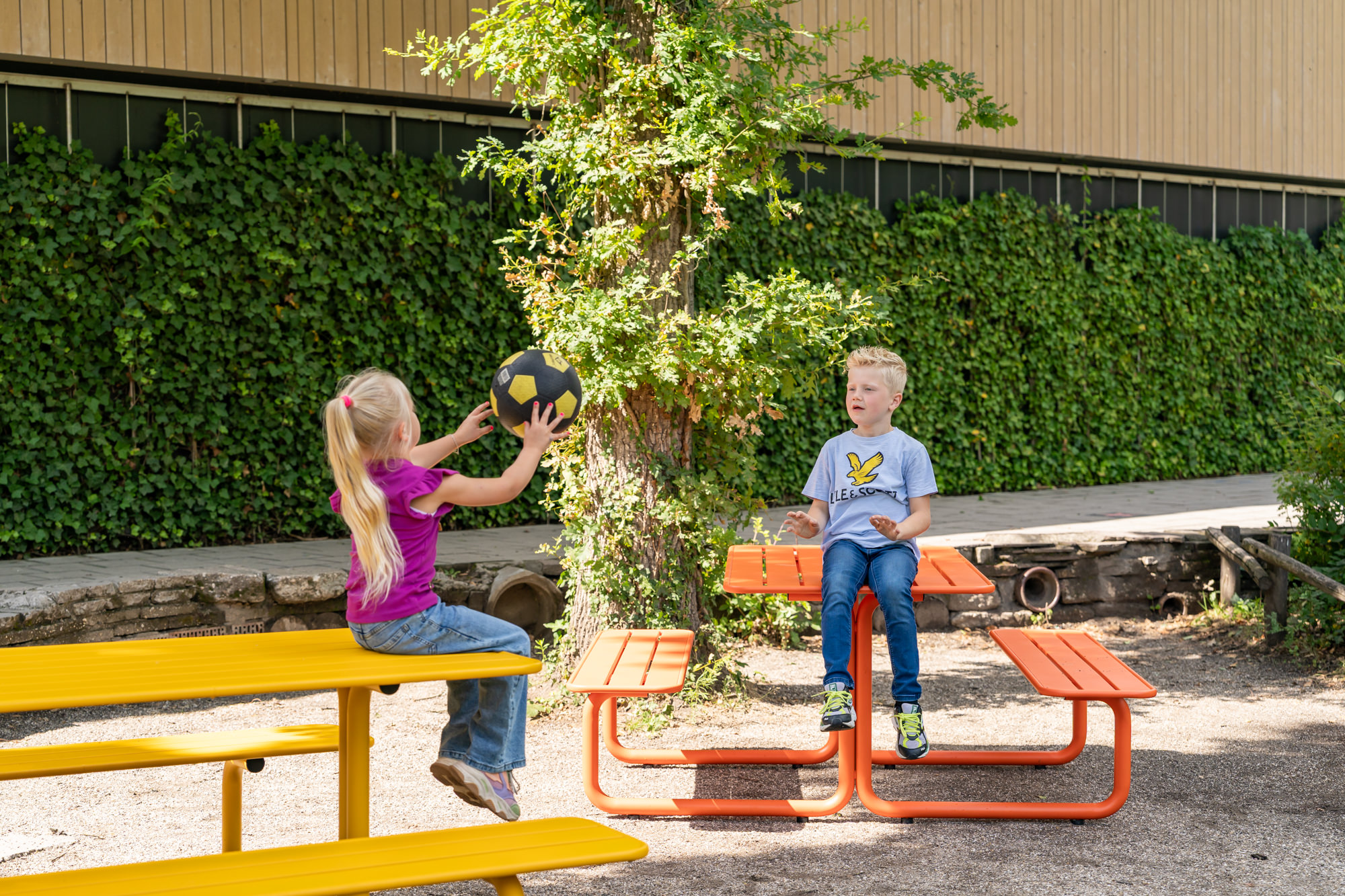 Spelende kinderen aan gekleurde metalen picknicktafels 