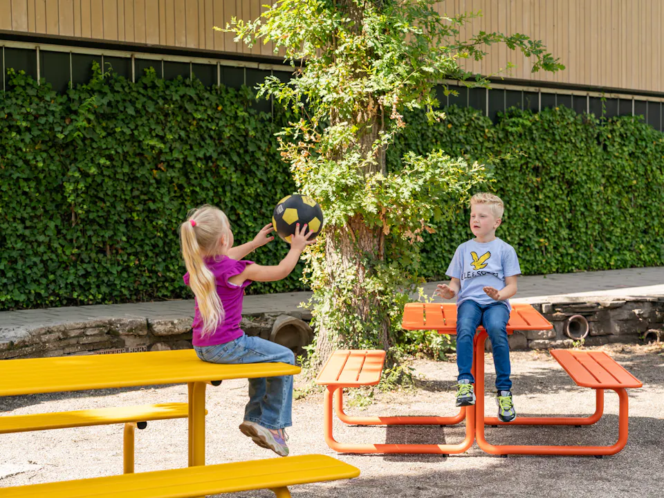Spelende kids aan gekleurde metalen picknicktafels