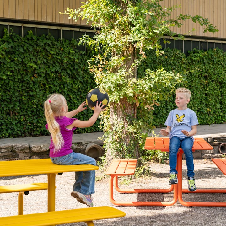 Spelende kids aan gekleurde metalen picknicktafels