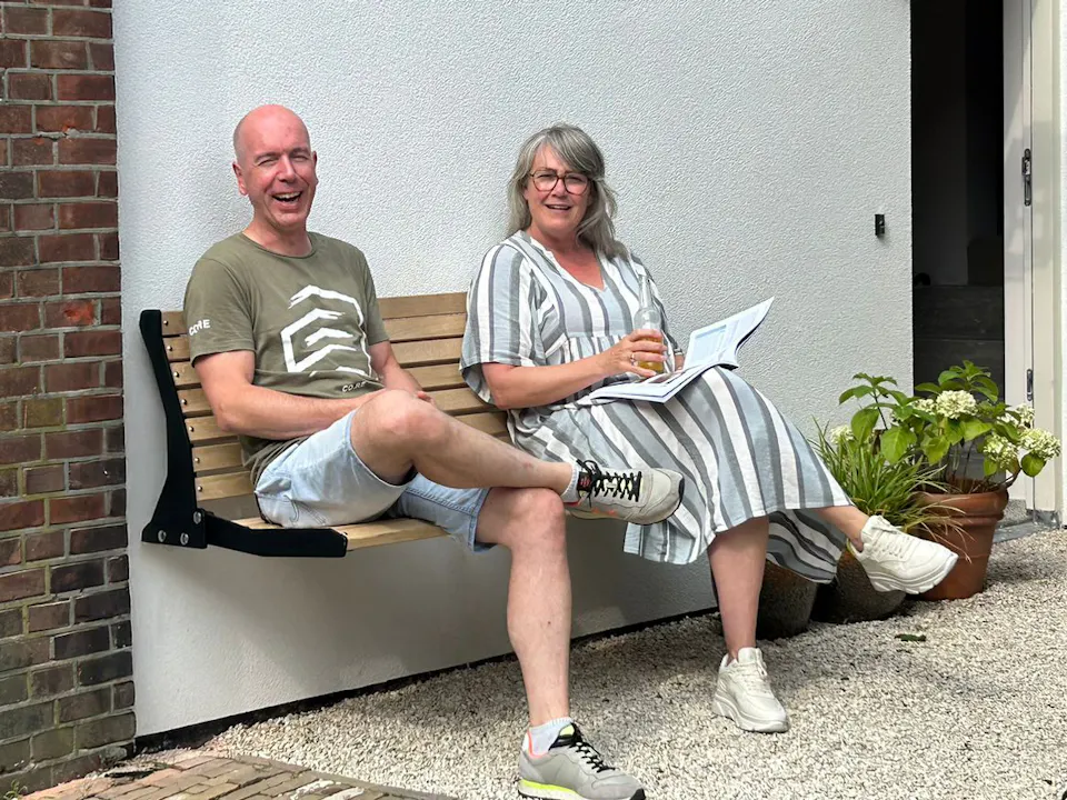 Couple sitting on a bench on the façade in the Jordaan, on the side of the house
