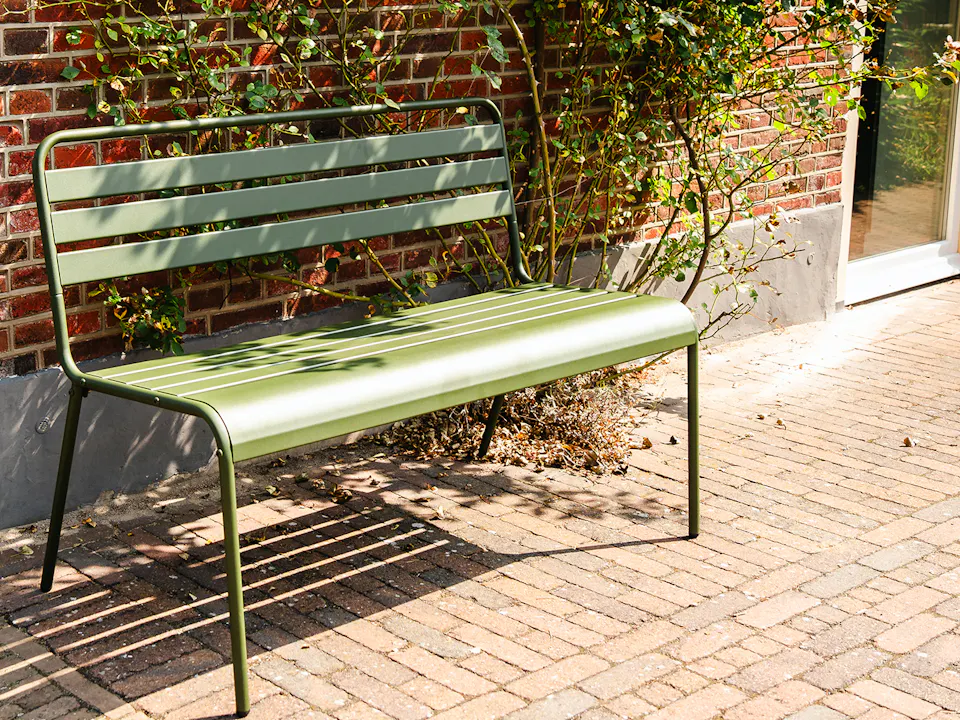 Olive-green metal garden bench by the house
