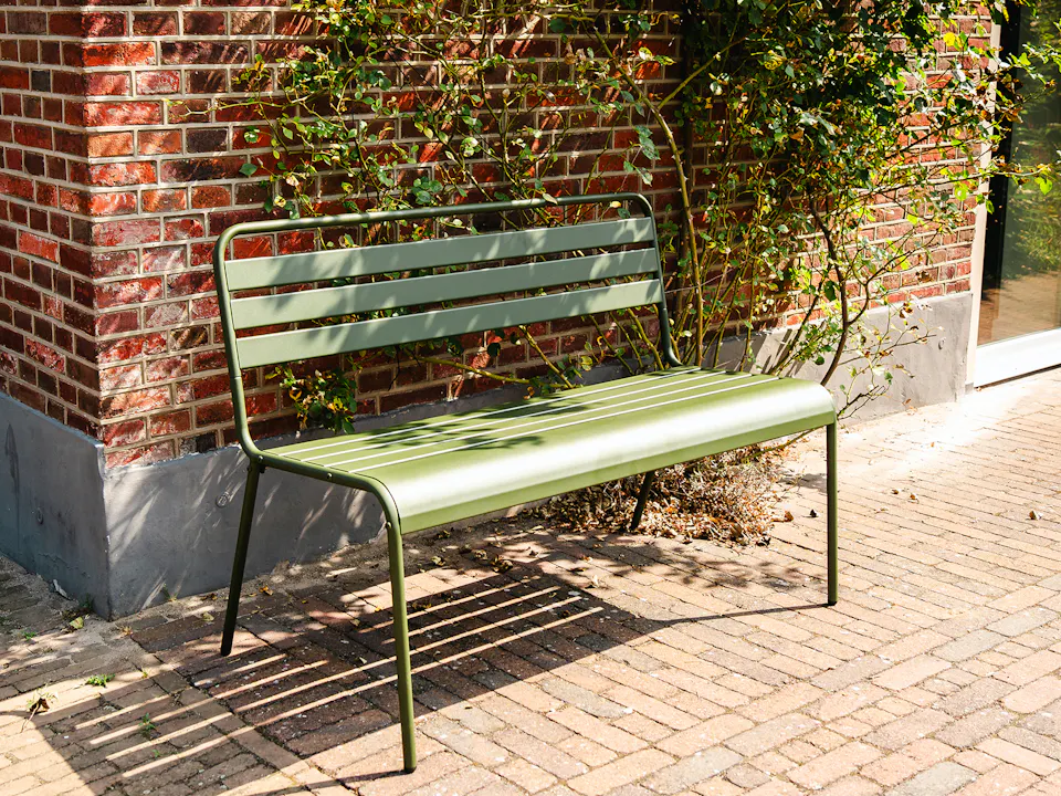 Olive-green metal garden bench by the house