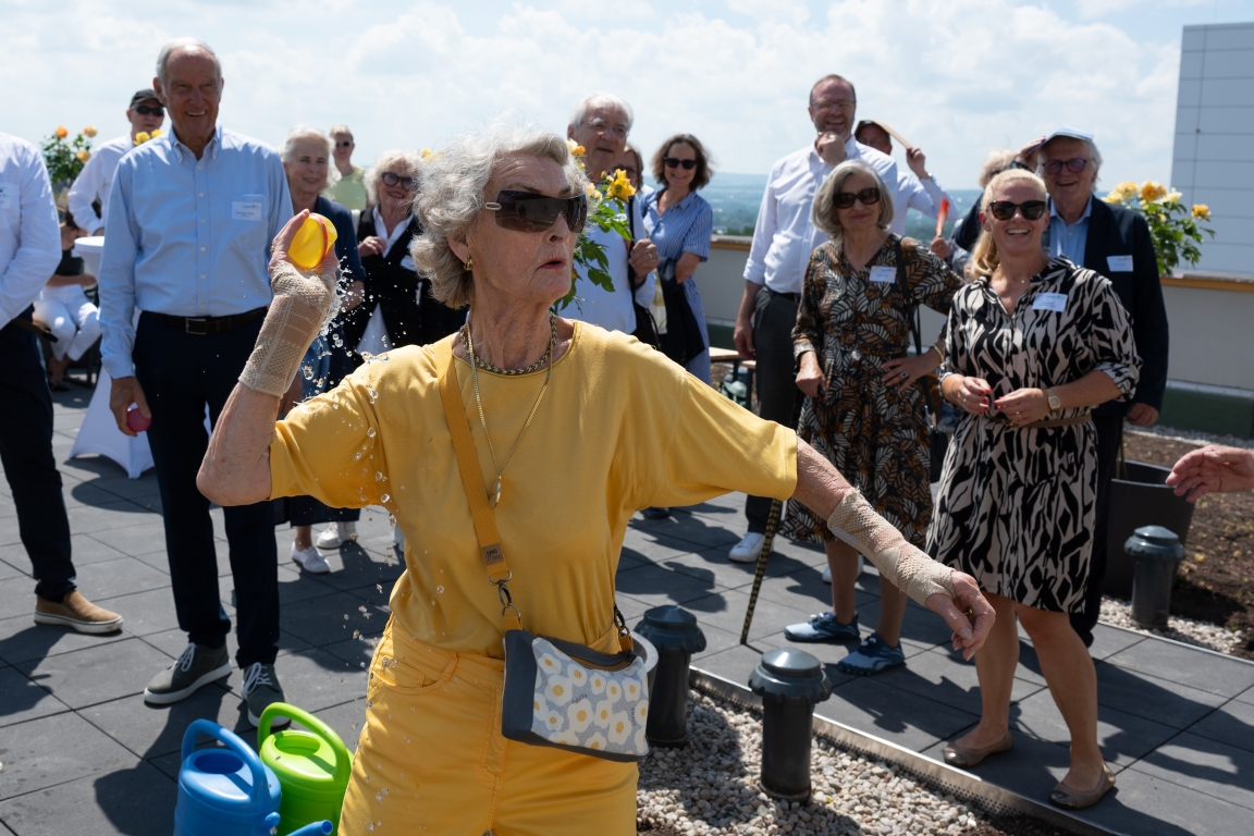Taufe mit Wasserbombe - Uta Neuhaus auf der Dachterrasse des im Juni 2026 fast fertiggestellten Apartmenthauses NeuHaus, benannt nach ihrem verstorbenen Mann Hermann.