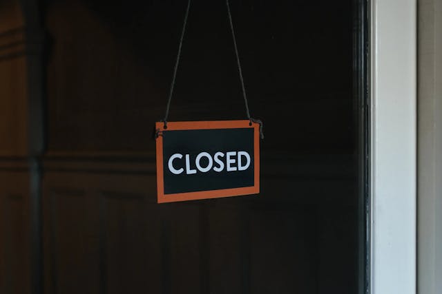 black rectangular sign with red edges hanging on door, with the word "closed"