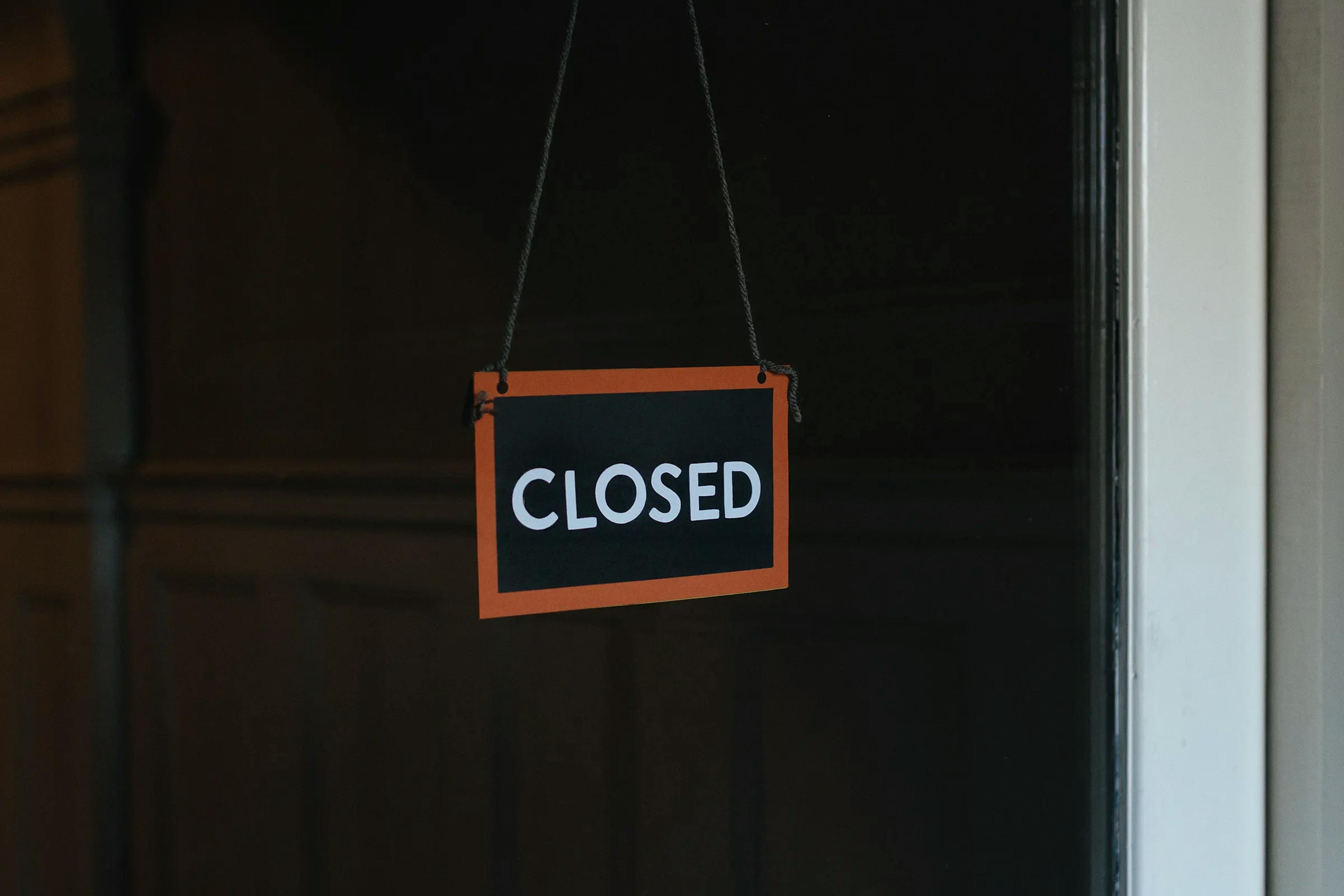 black rectangular sign with red edges hanging on door, with the word "closed"