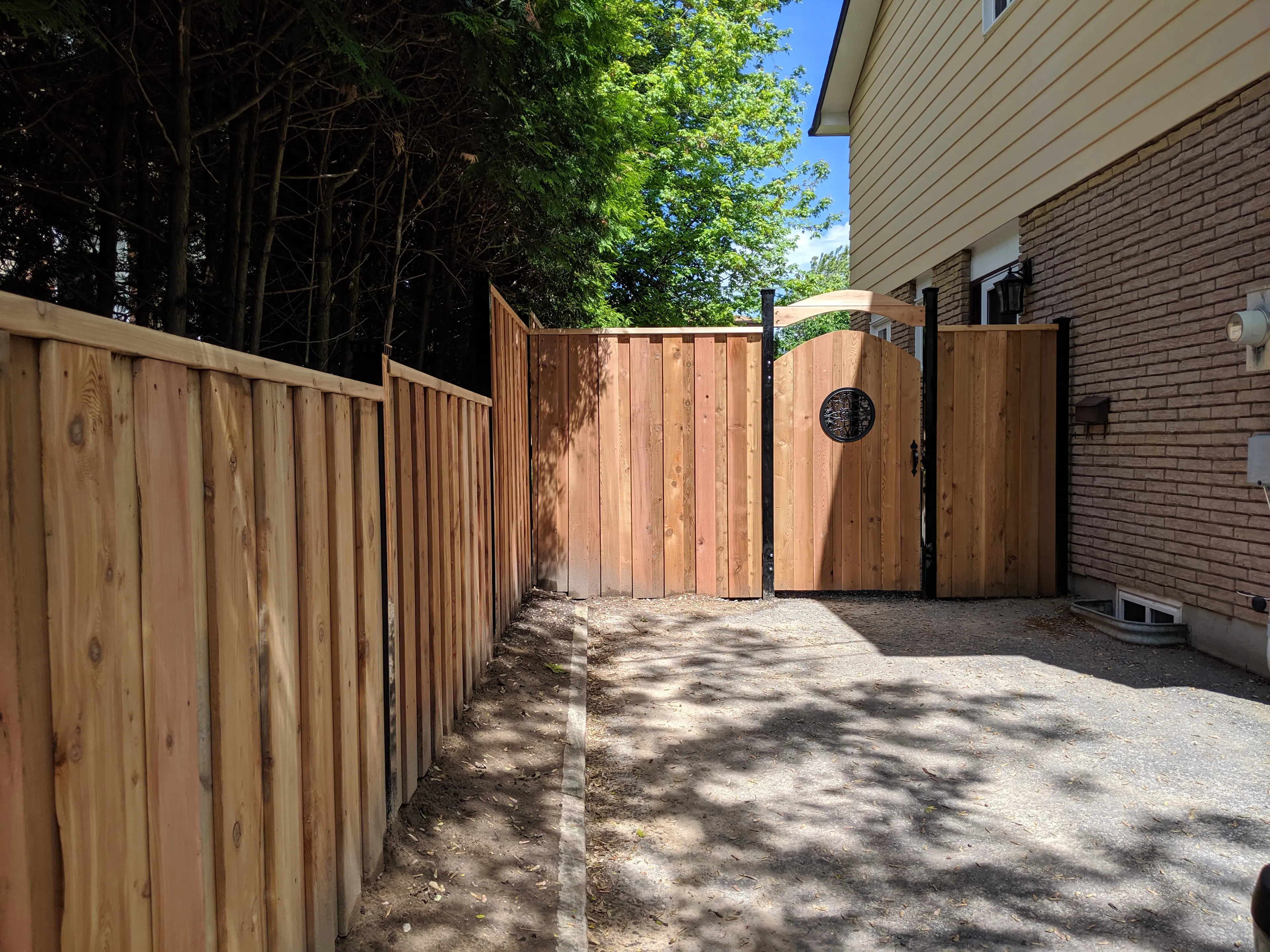 A wooden fence and a matching gate with a circular window, leading to a building on the right.