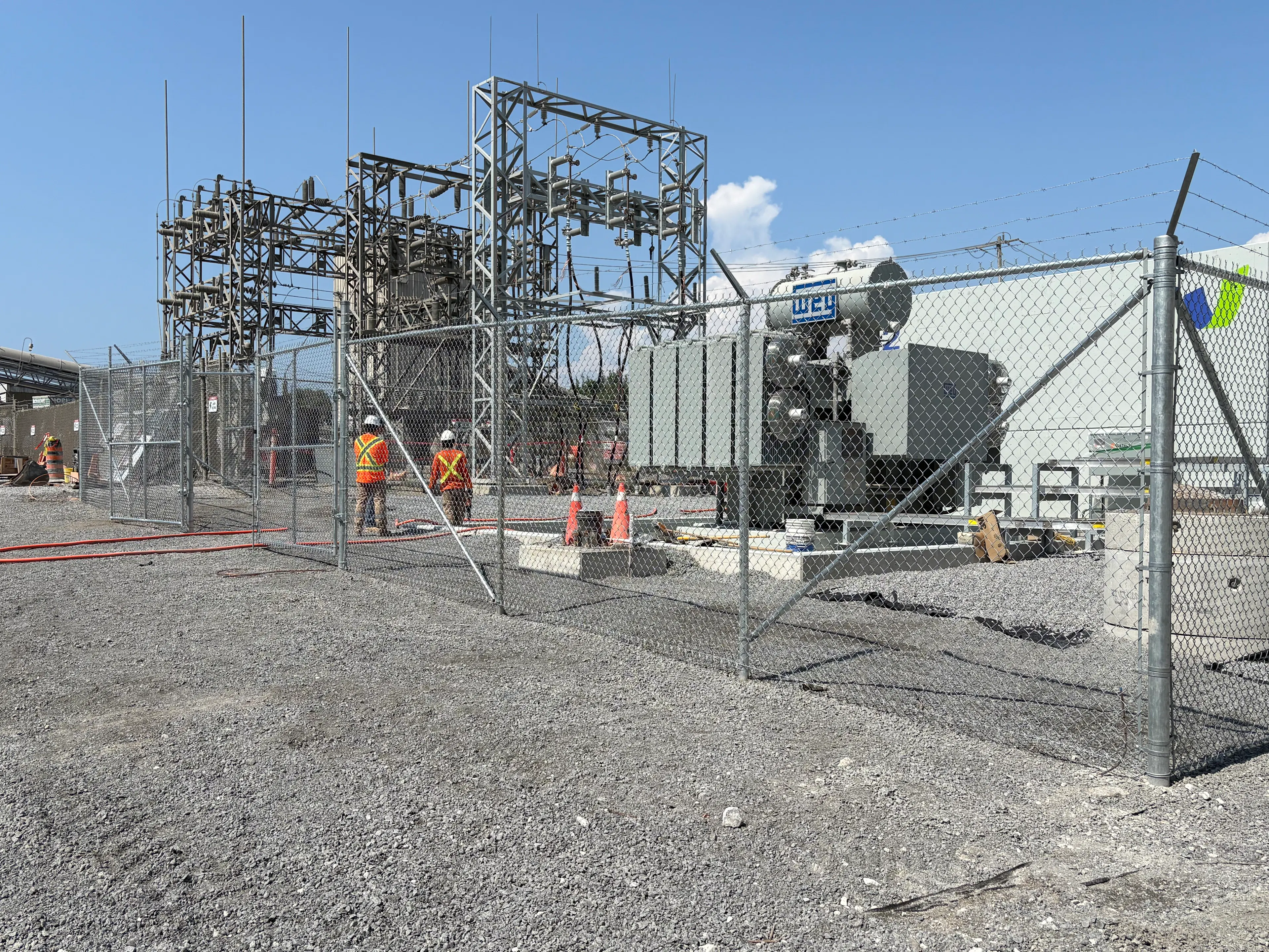 A commercial chainlink fence with barbed wire on the top enclosing an electrical power generator station.