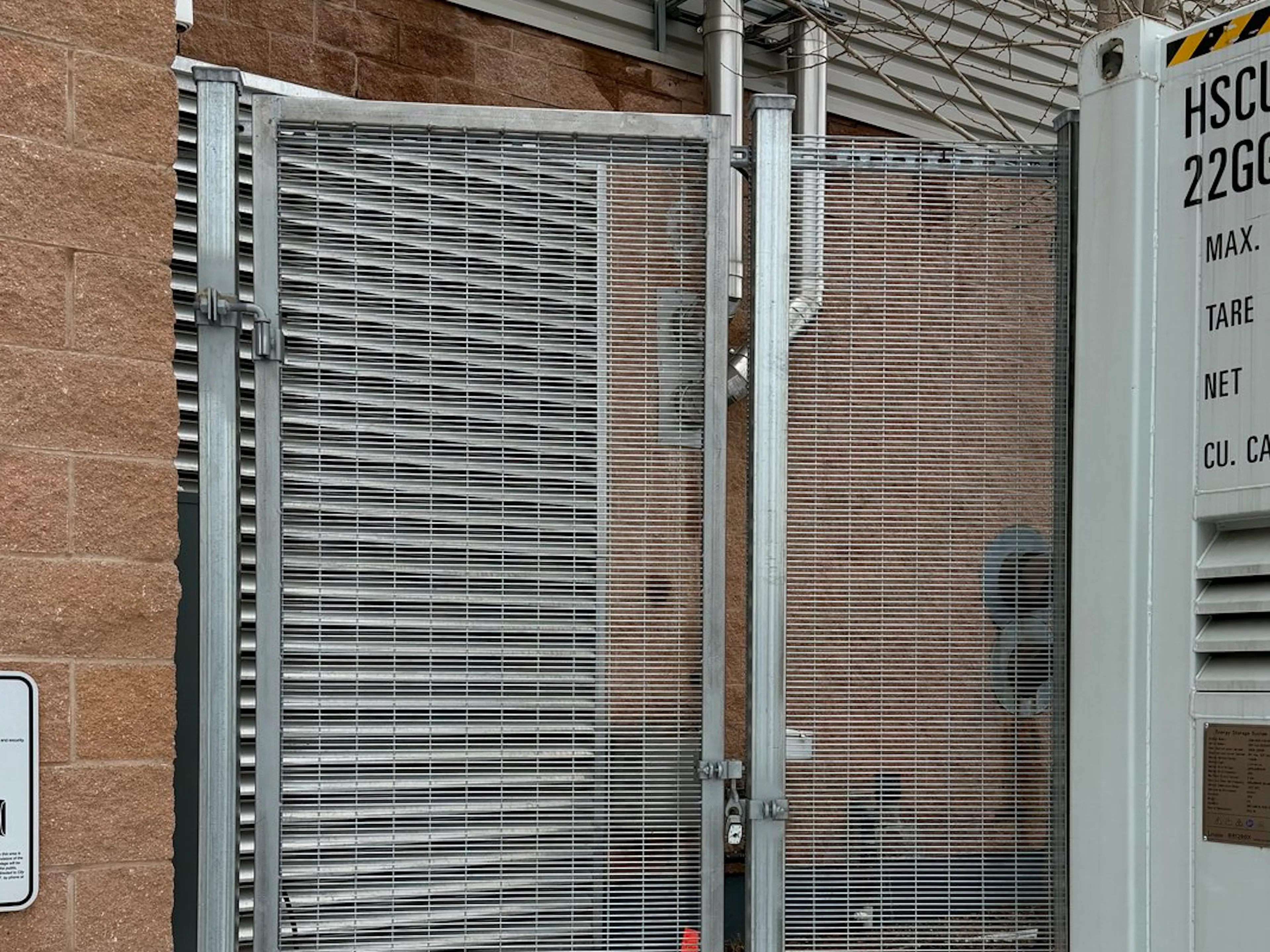 A grey commercial security gate, revealing a brick wall.