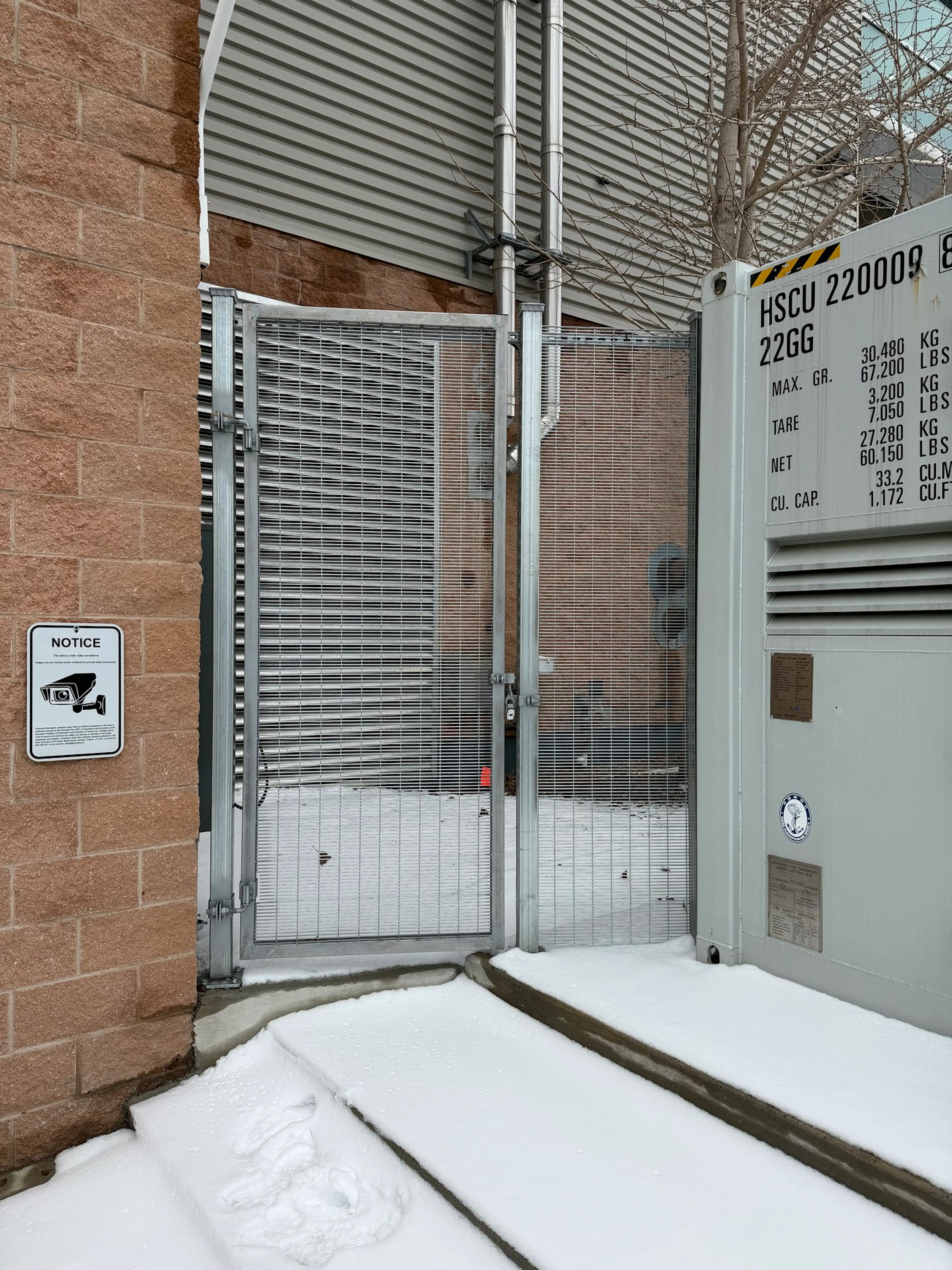 A grey commercial metal gate with a mesh screen stands between a brick wall.