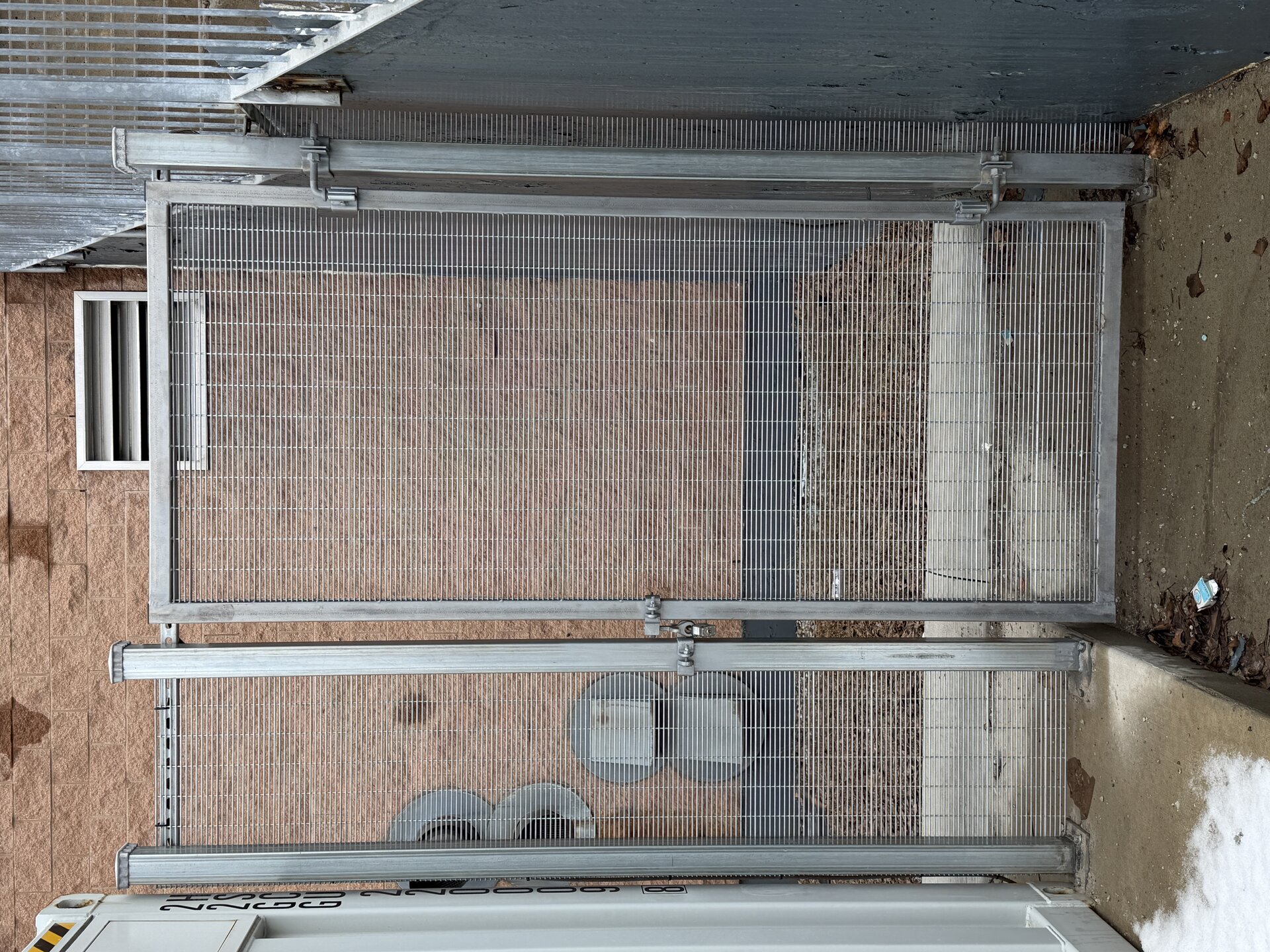 A grey commercial high-security gate with a mesh screen in front of a brick wall.
