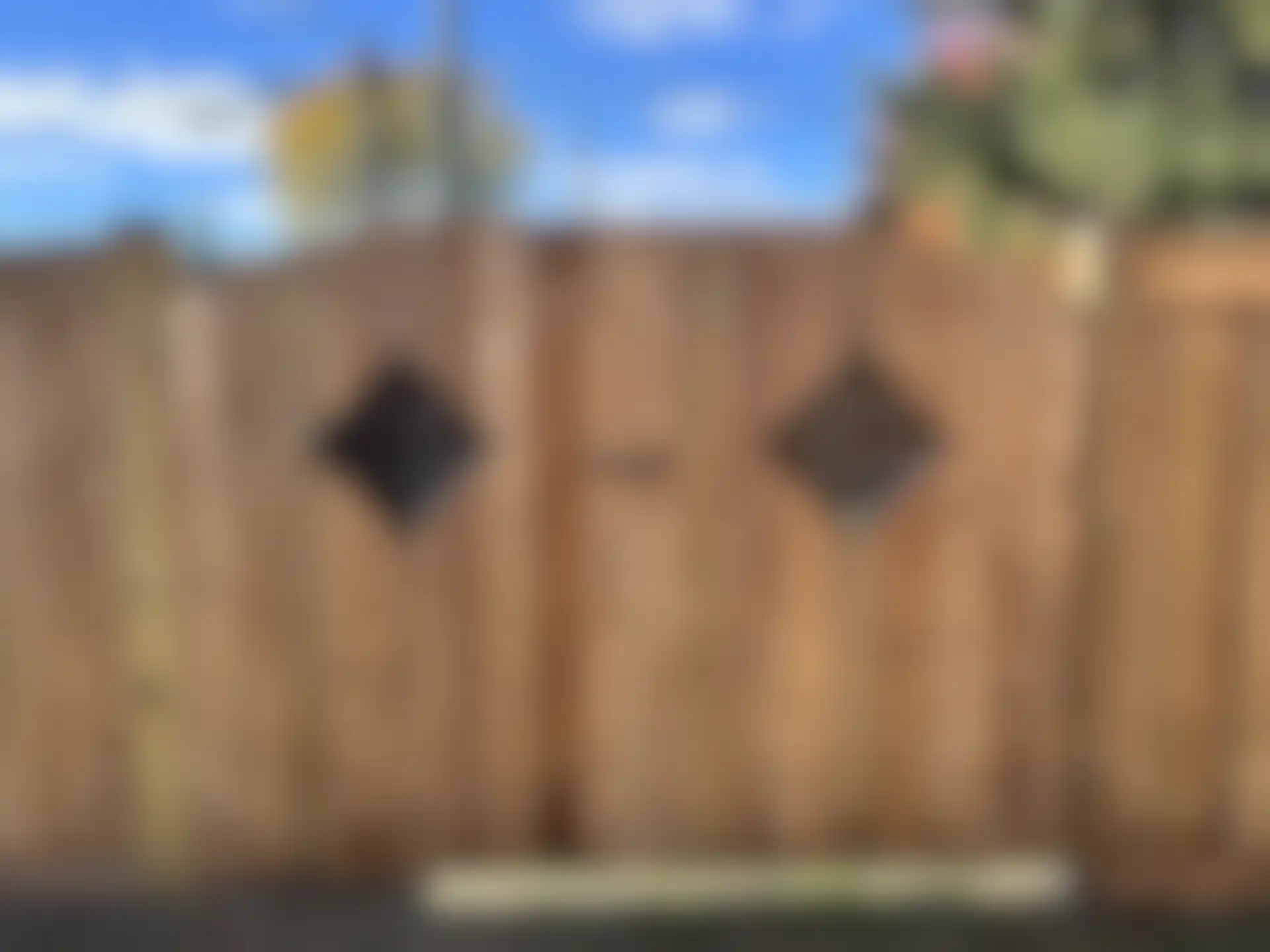 A wooden backyard gate with two diamond-shaped metal inserts and a black handle in the center of the fence gate.
