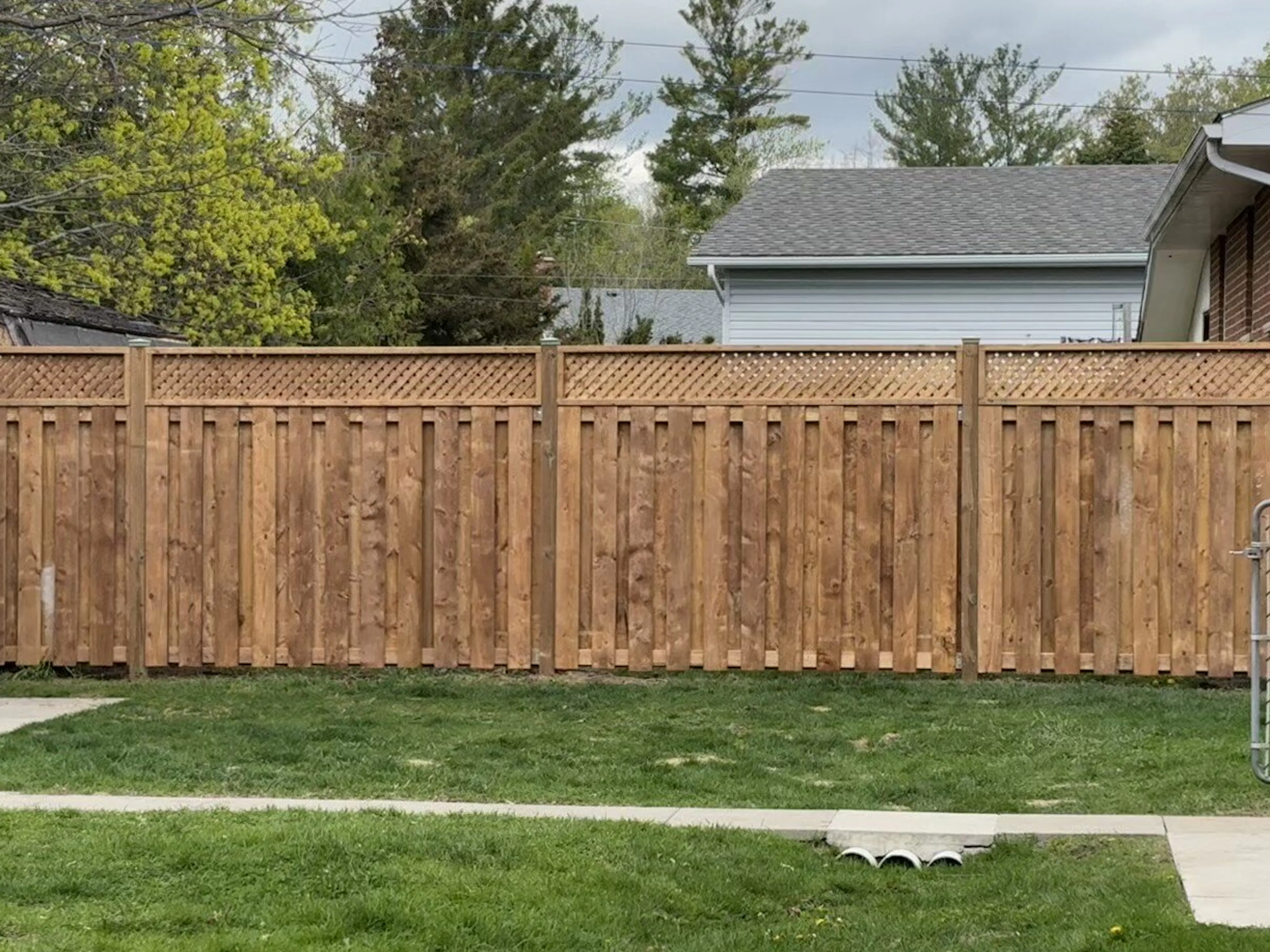 A newly constructed wooden privacy fence with decorative cutouts at the top runs along a grassy yard.