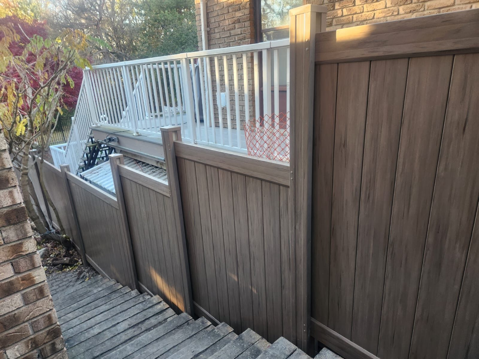 A brown vinyl fence next to a set of outdoor stairs in a residential backyard.