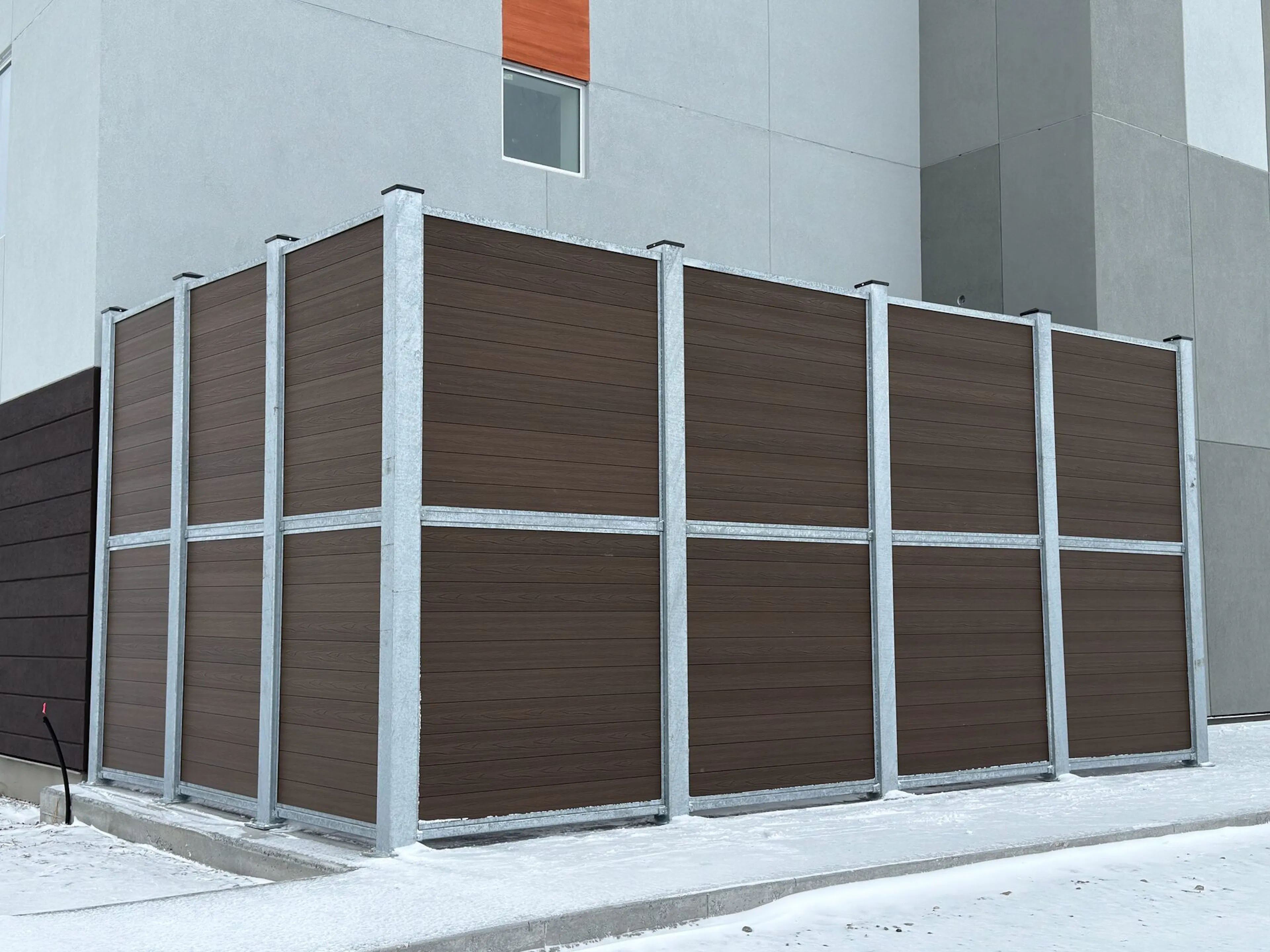 A tall brown vinyl fence with a silver frame stands against a building.