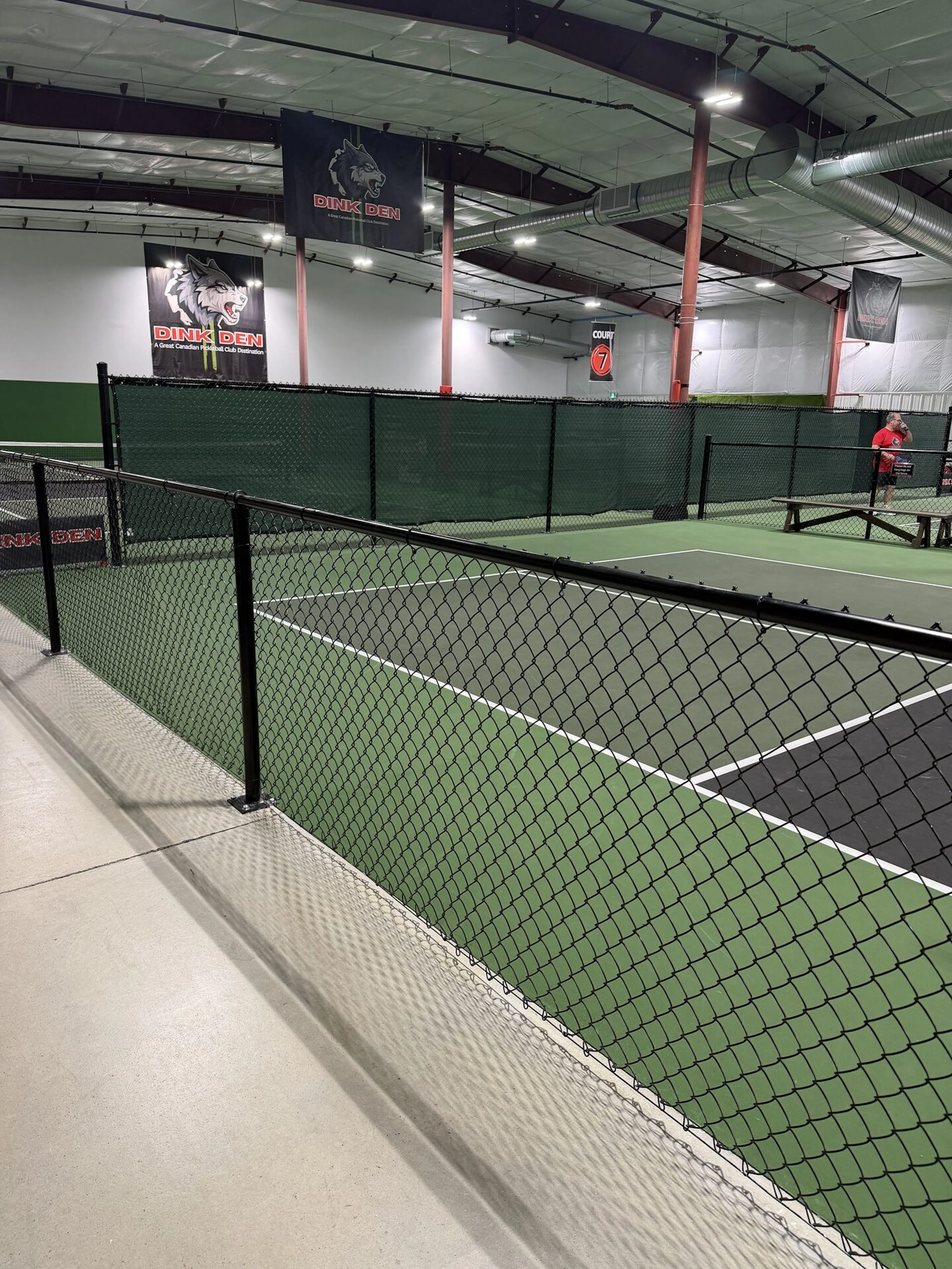 An indoor pickleball facility with green turf courts and black chain-link fencing.