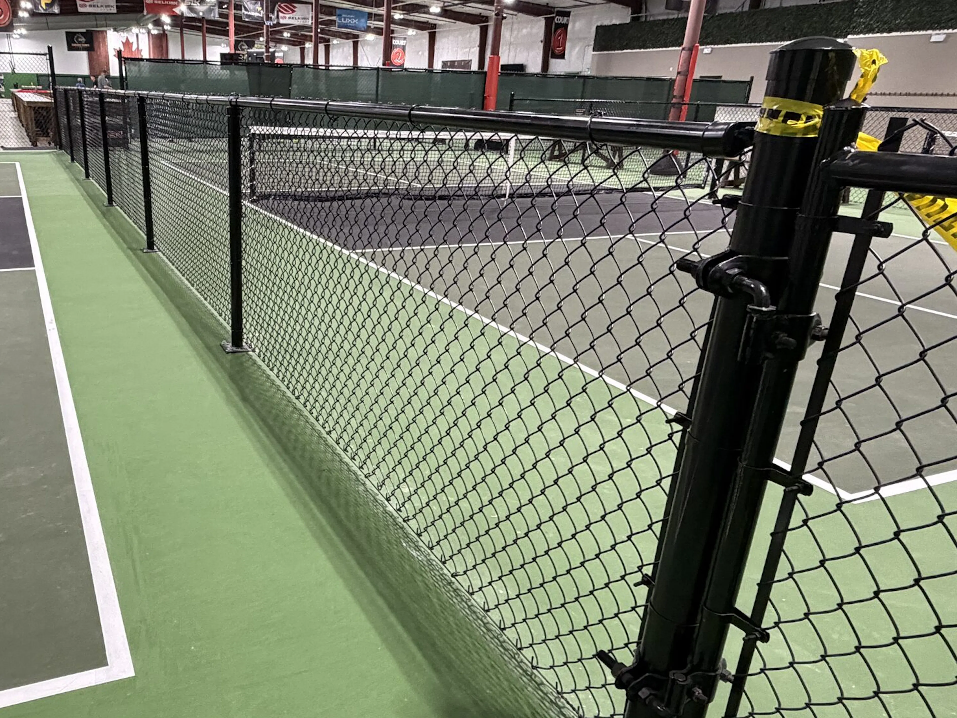 An indoor pickleball court with green flooring and black chainlink fencing.