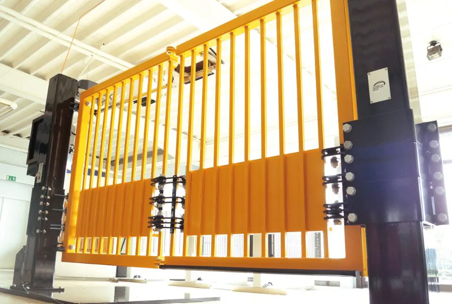 A large yellow metal security gate with vertical bars is installed indoors, supported by black metal beams and hinges, under a white ceiling with exposed beams.