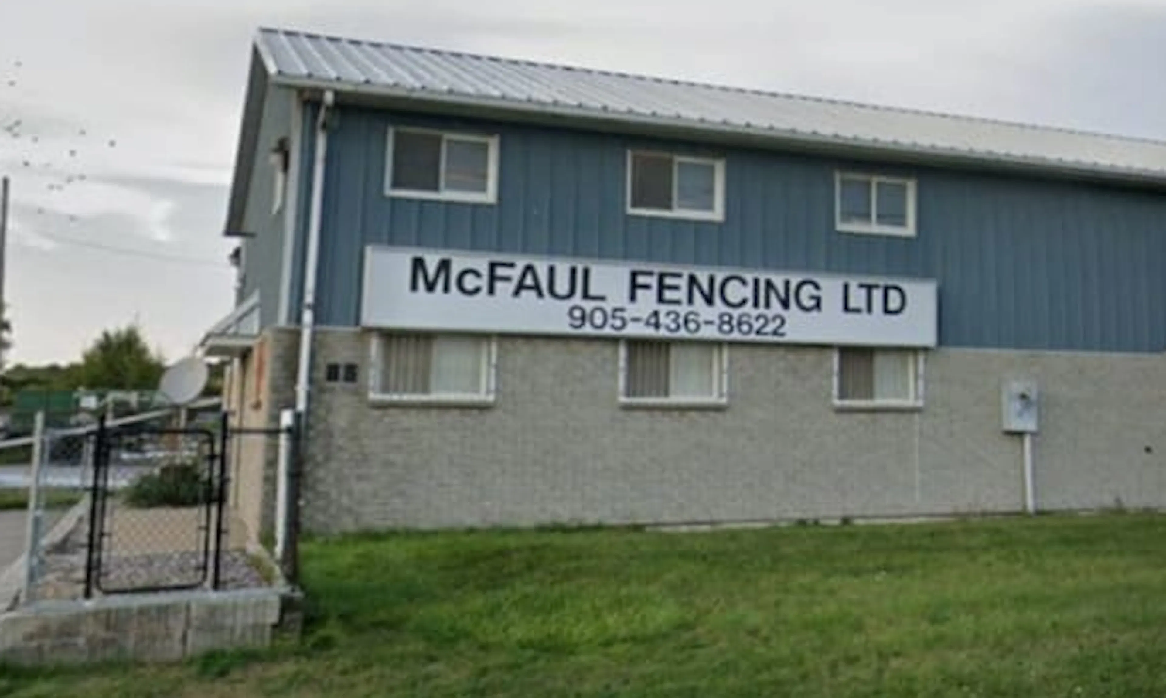 A two-story building with a large sign reading "McFAUL FENCING LTD 905-436-8622" on its exterior wall.