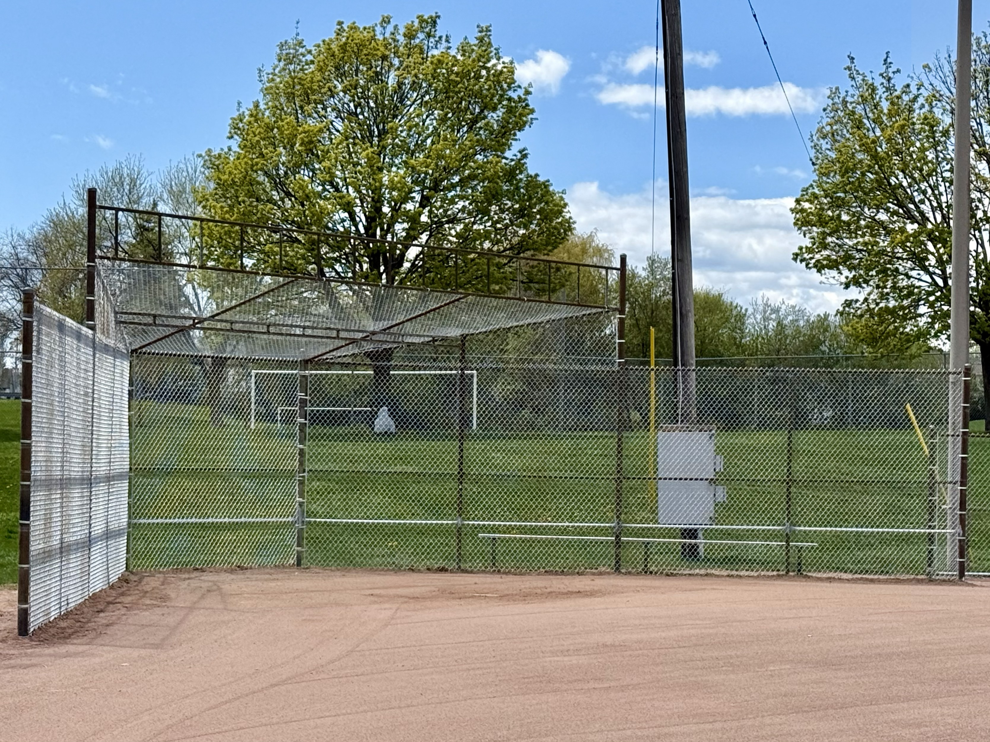 A gray chain-link fence surrounds a baseball field with a dirt infield and grass outfield.