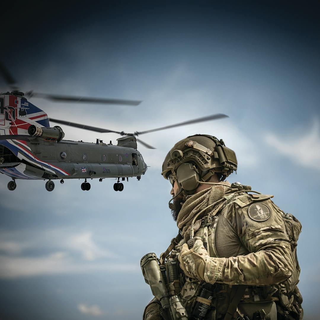A soldier in camouflage looking up at a British helicopter