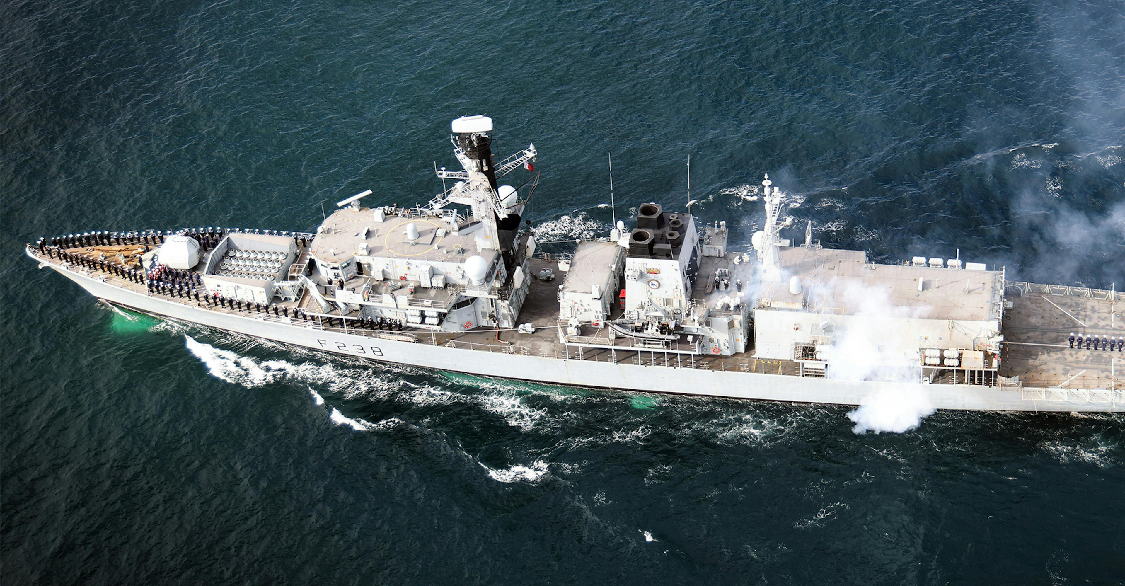 An aerial view of a navy ship sailing gracefully on the water, showcasing its strength and power.