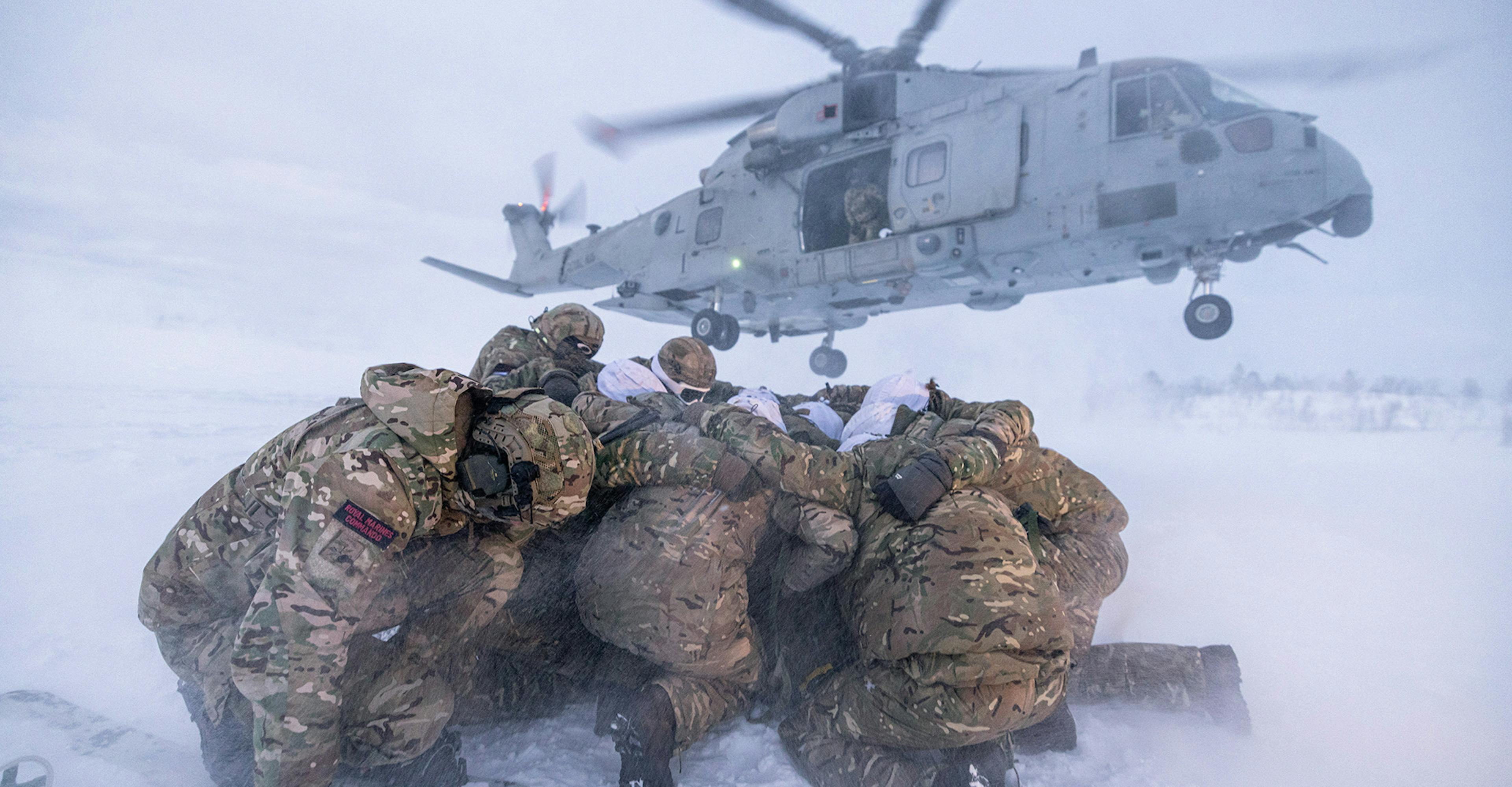 Soldiers in snow with helicopter in background.