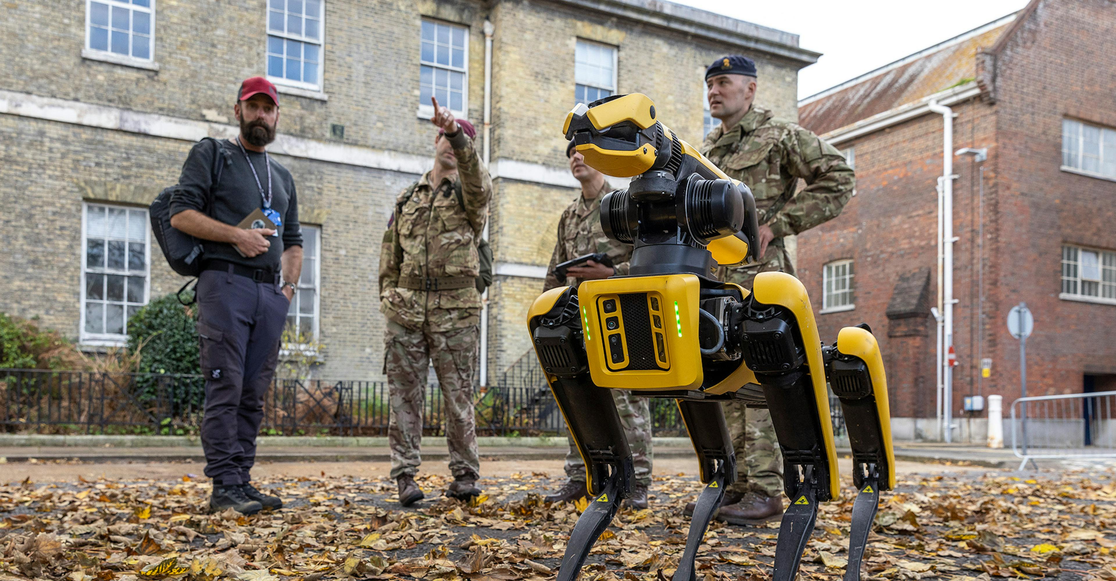 A man and two soldiers standing next to a robot, showcasing human-robot collaboration in military operations.