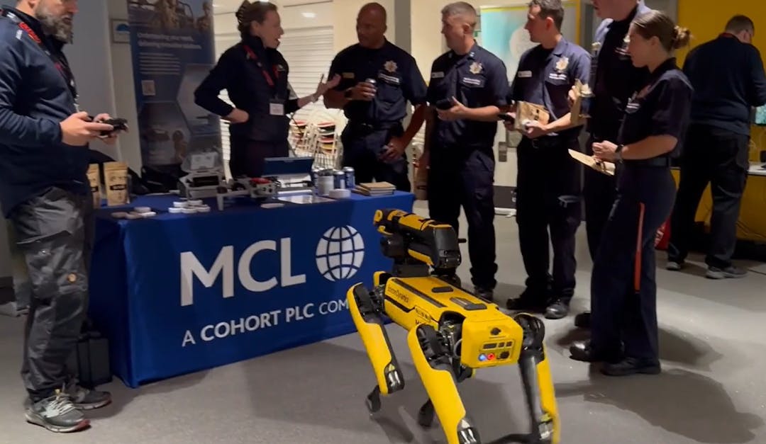 Group of uniformed emergency personnel gather around MCL company display with yellow quadruped robot (Spot) in foreground.