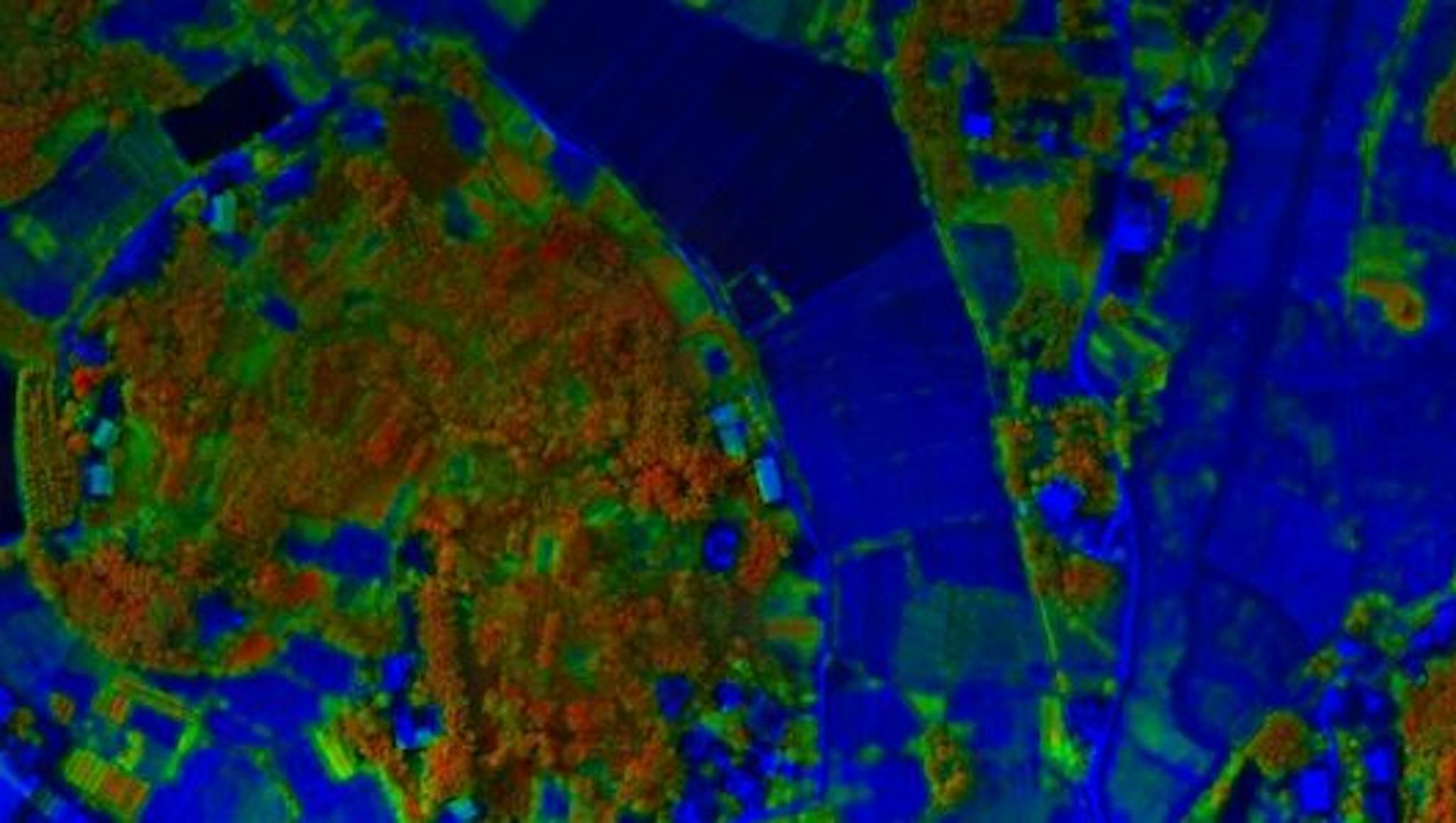 Infrared aerial view of farmland with patches of red and green vegetation against a deep blue landscape, highlighting field patterns and foliage contrast.