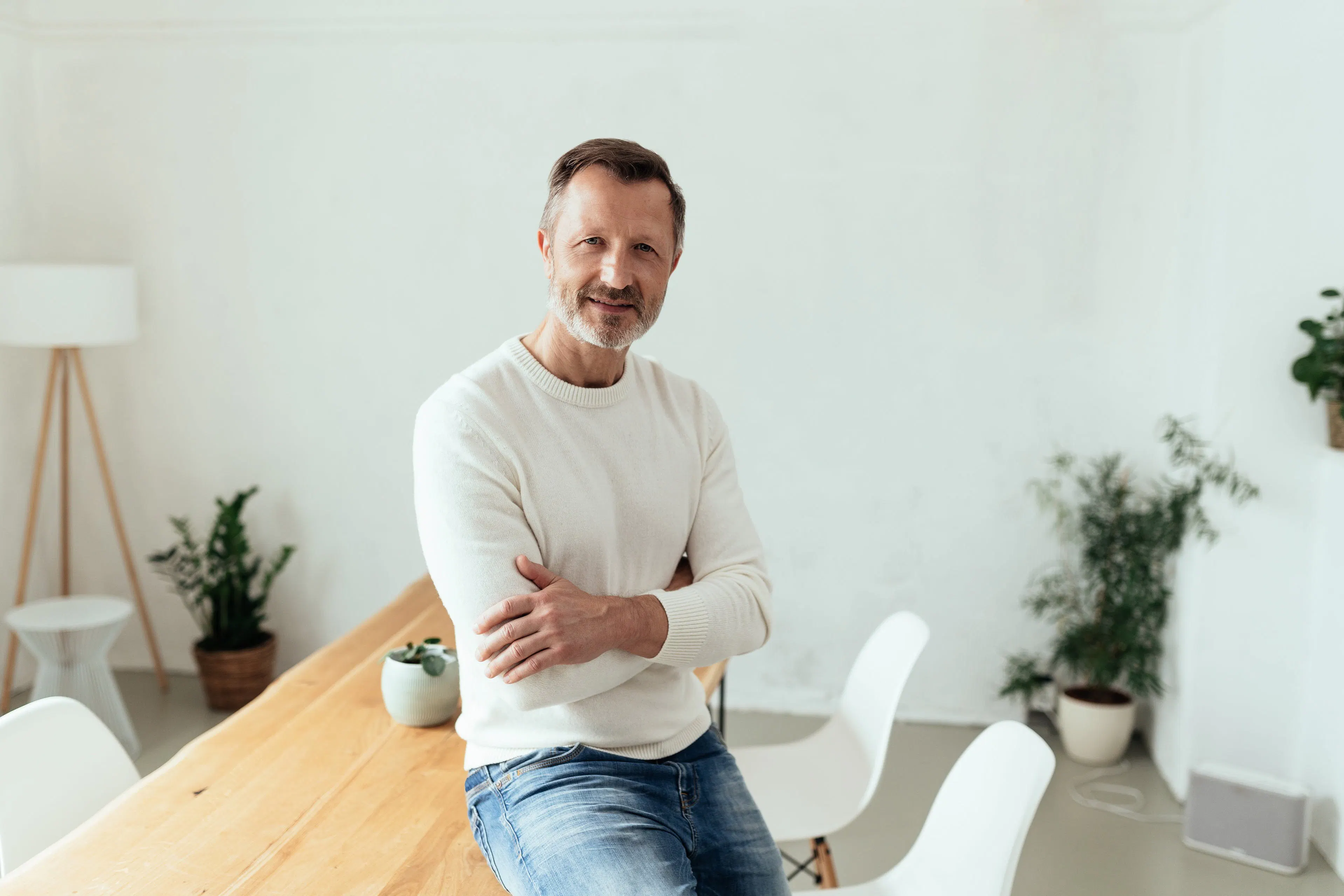Man in white jumper leans on a desk