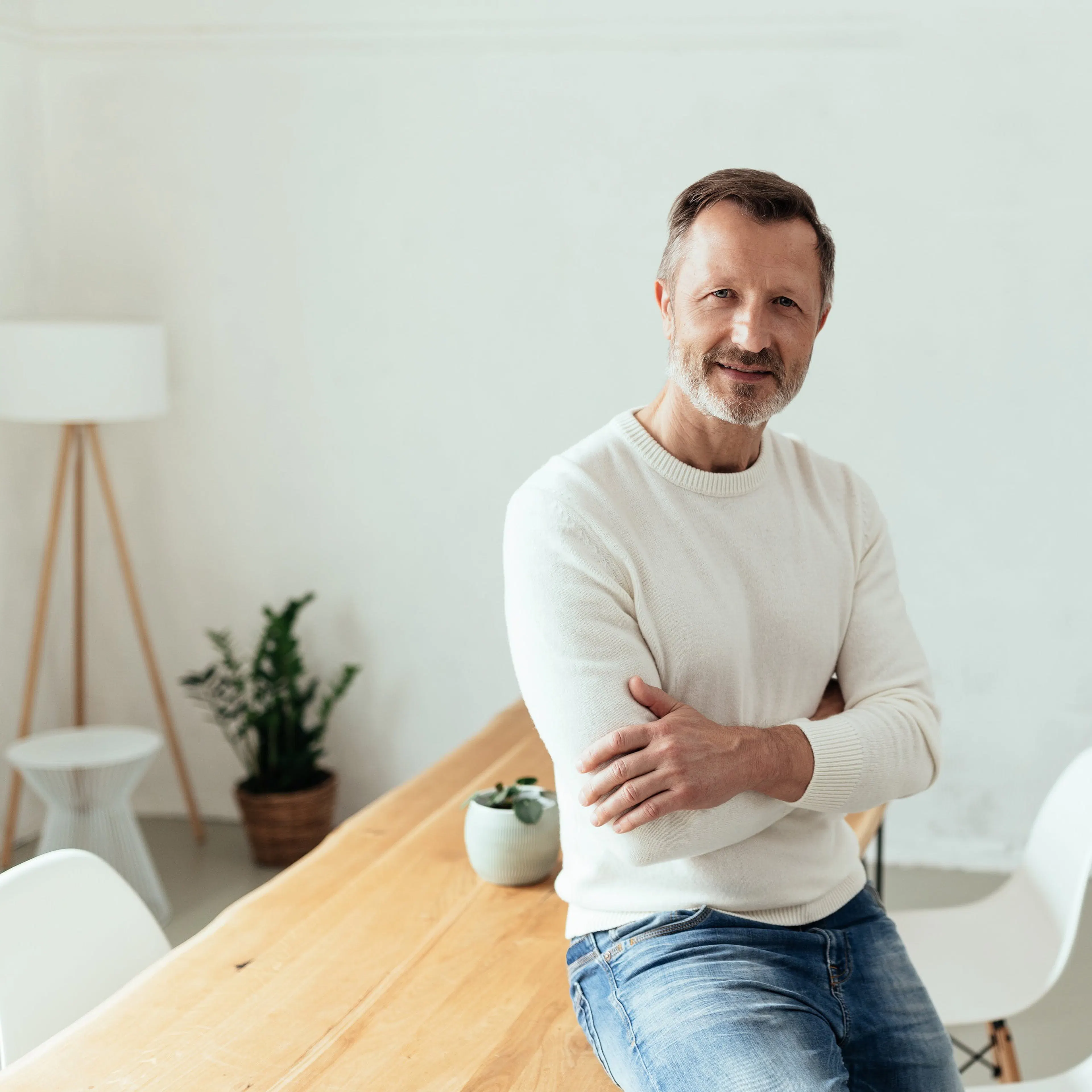 Man in white jumper leans on a desk