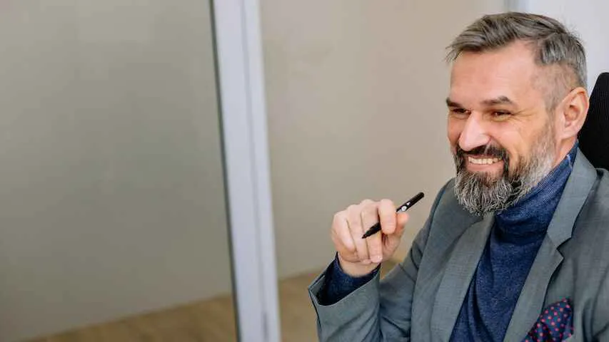 Man in a blue polo neck sitting at a desk with a pen in his hand