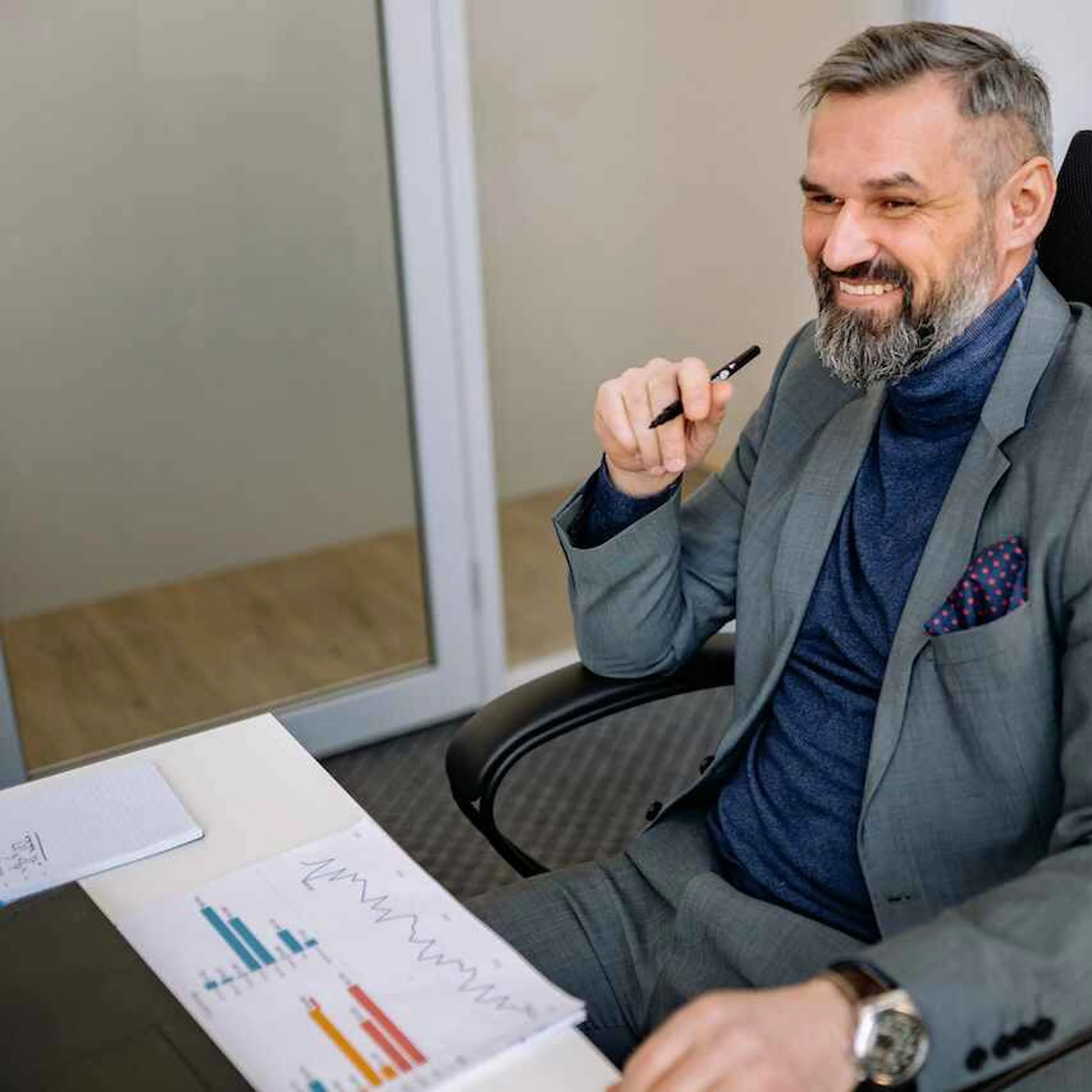 Man in a blue polo neck sitting at a desk with a pen in his hand