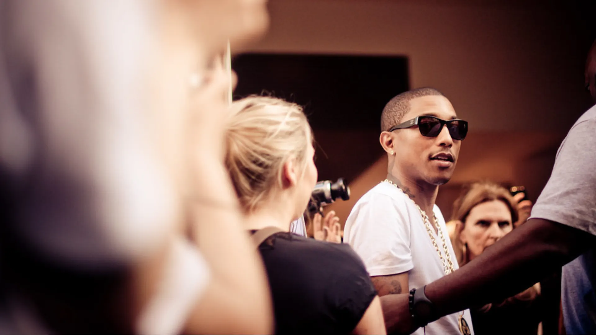 Pharrell Williams with sunglasses on surrounded by crowd