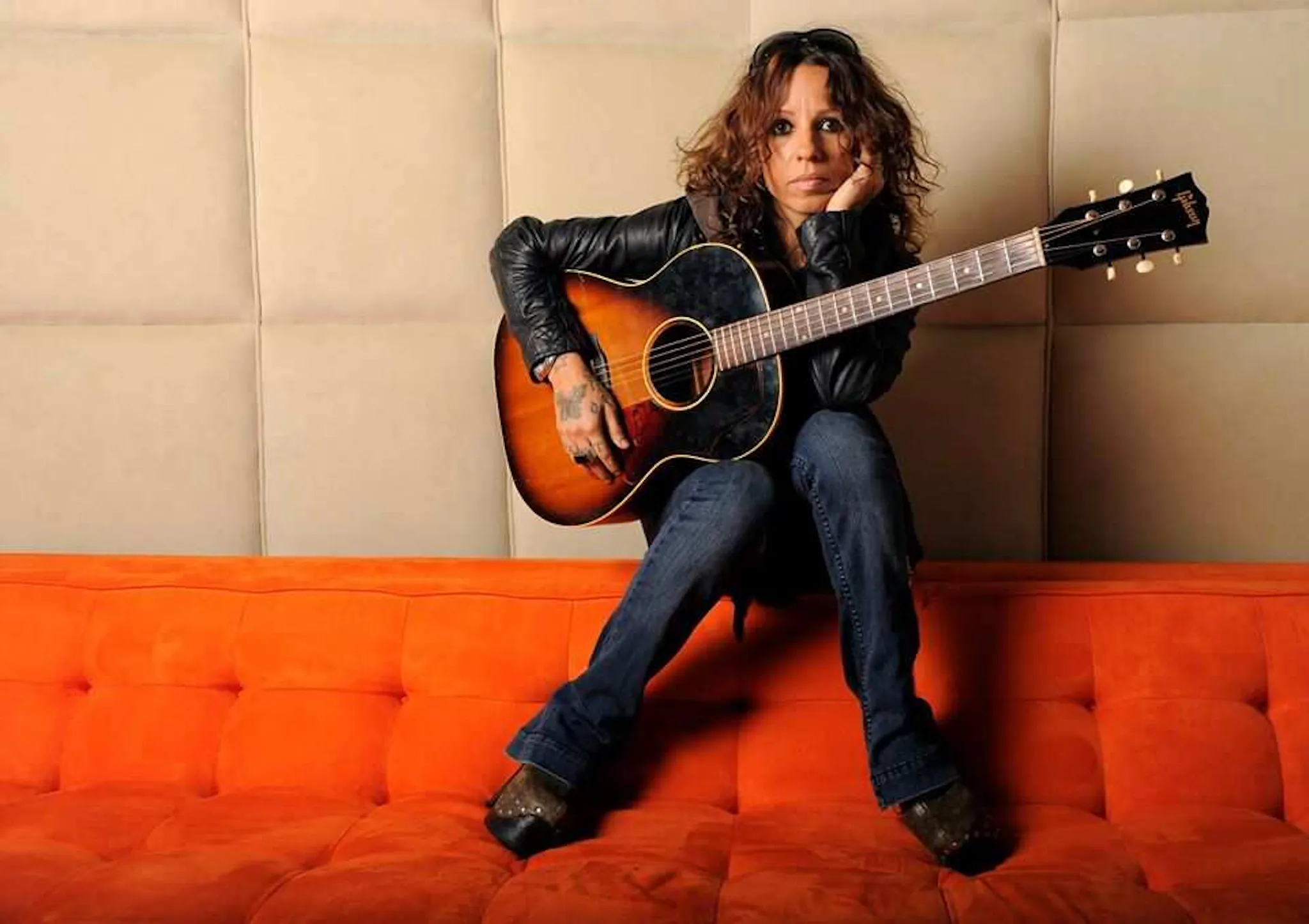Linda Perry sat on back of sofa with acoustic guitar