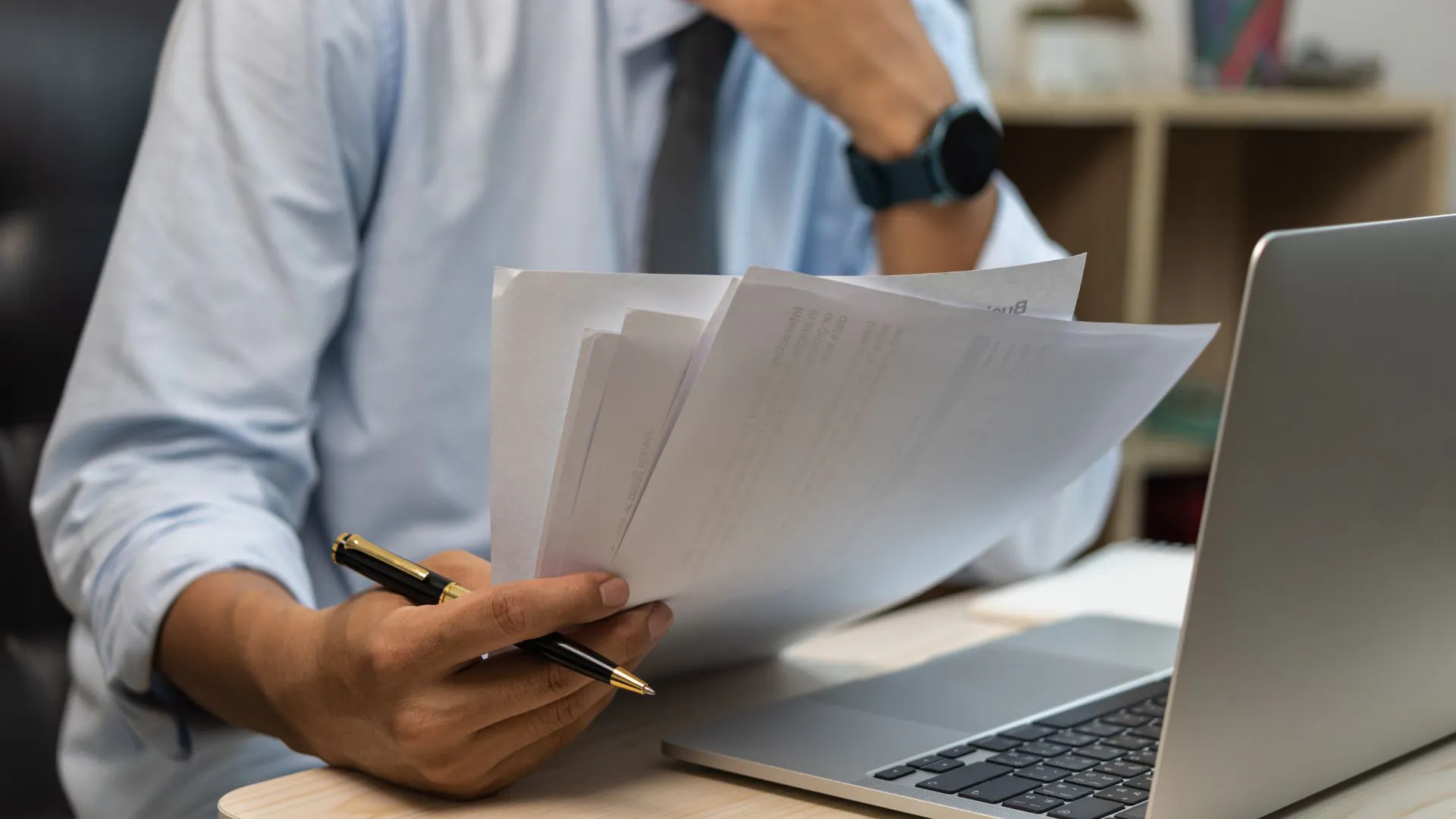 Male hand holding papers looking at laptop