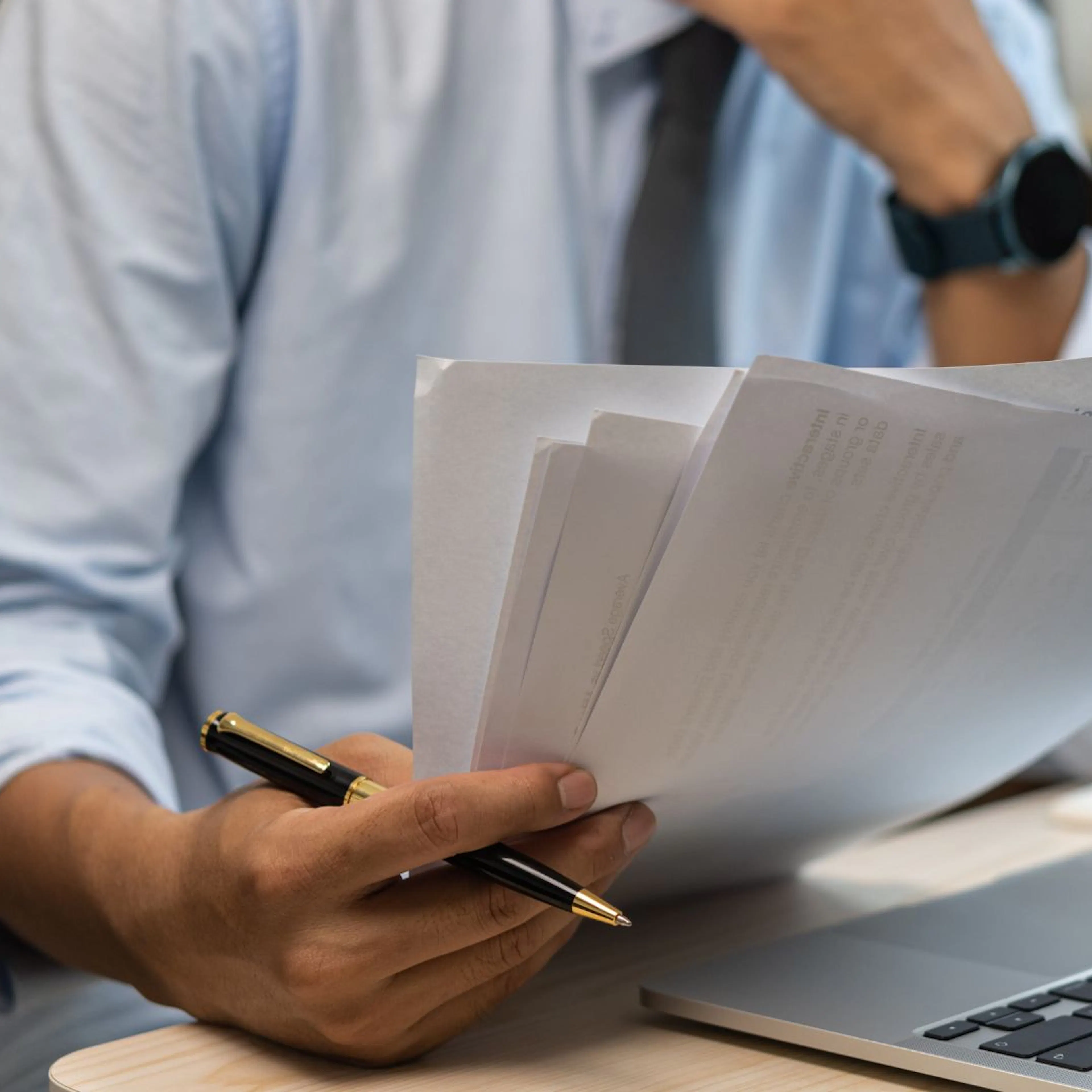Male hand holding papers looking at laptop