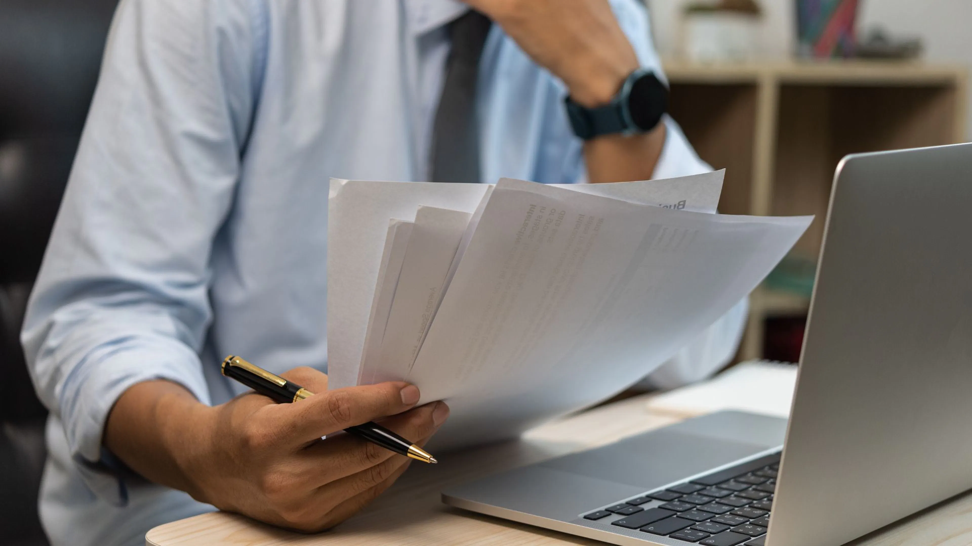 Male hand holding papers looking at laptop