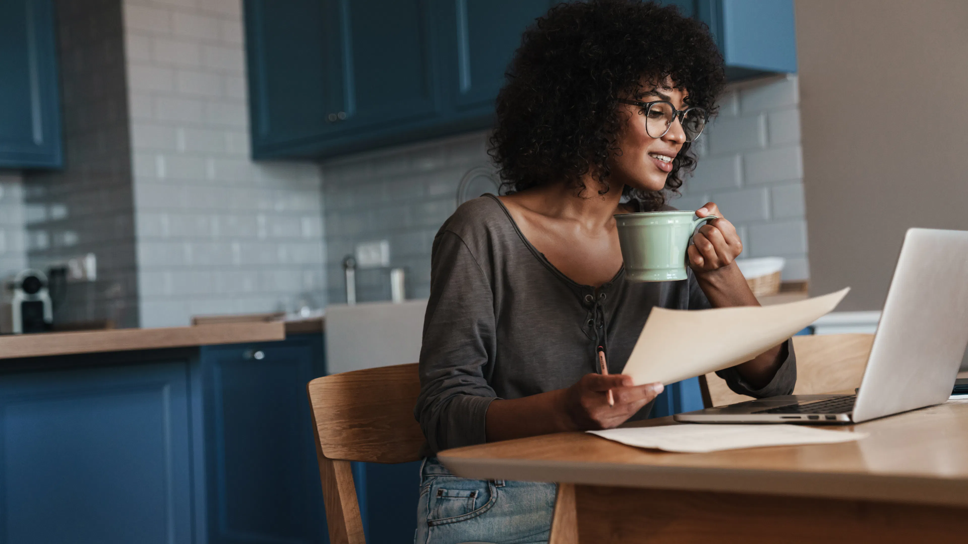 Female working from kitchen table with laptop and paperwork 