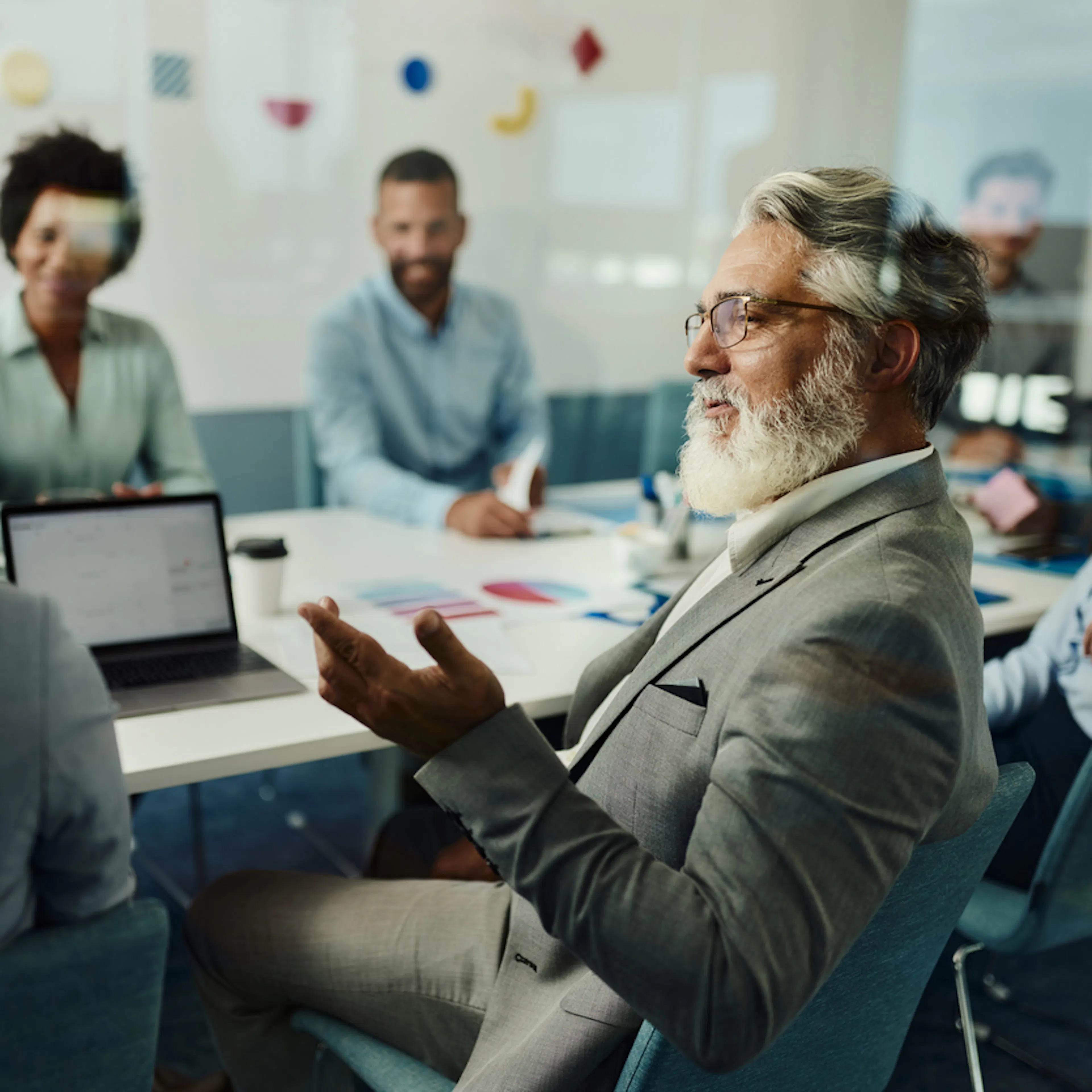 Man in office looking at woman explaining something from laptop, middle aged, glasses, white beard